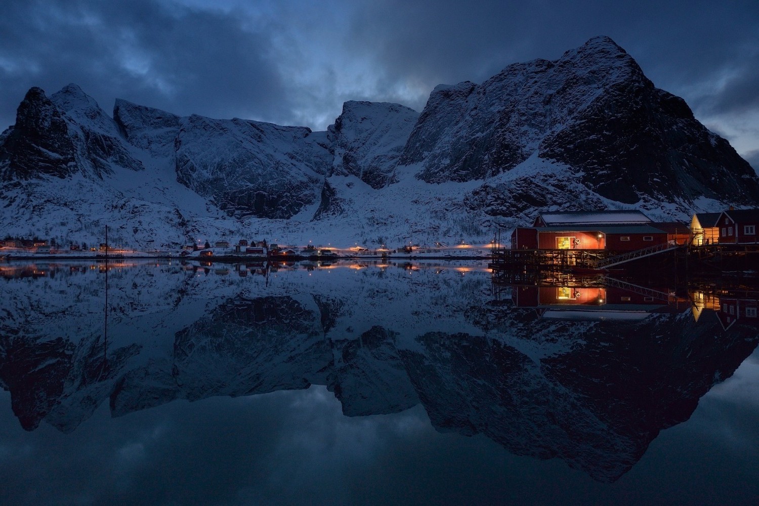 Winter village with snow-capped mountains reflected in a calm lake HD Wallpaper