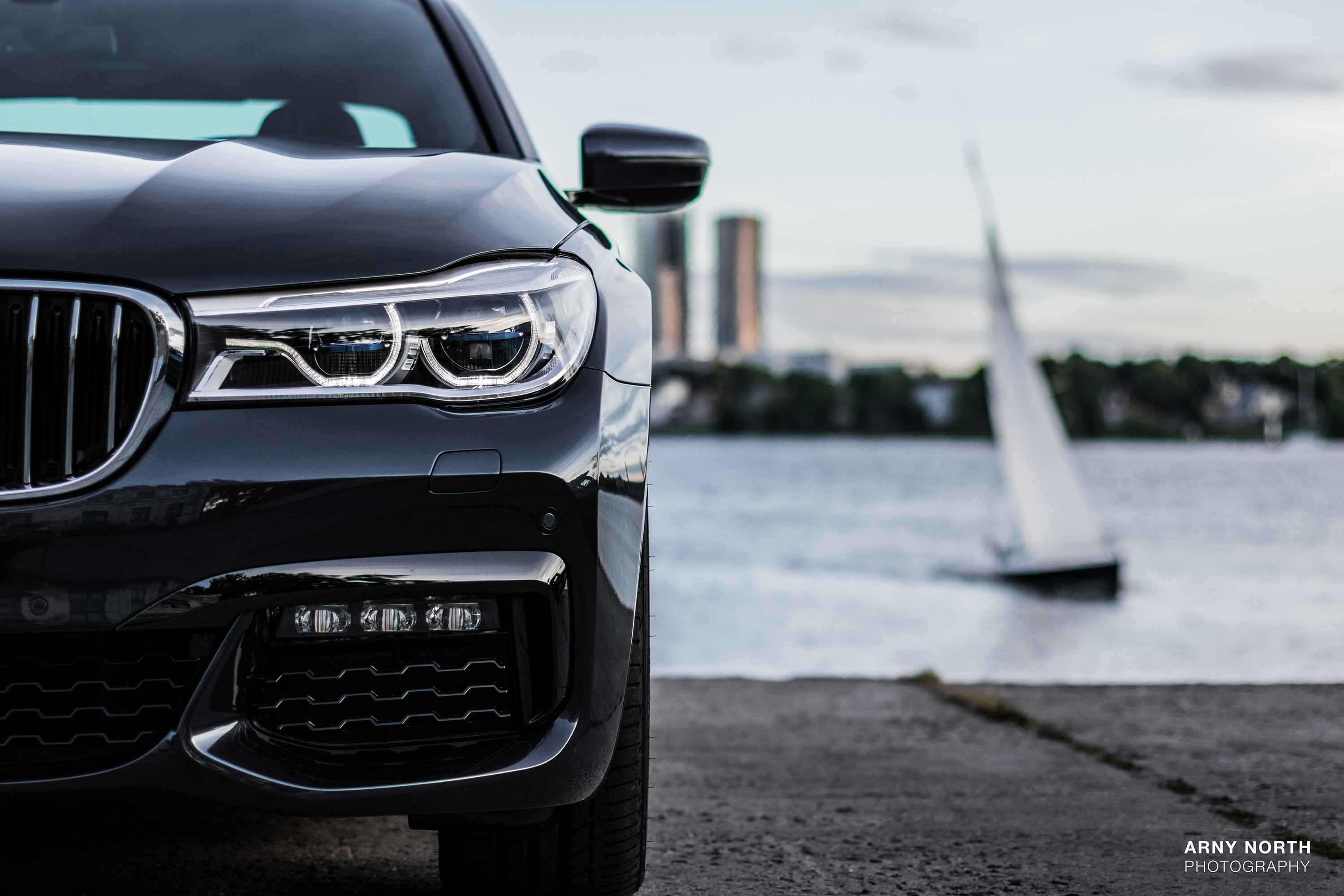 Black BMW 7 Series car by the water with a sailboat HD Wallpaper