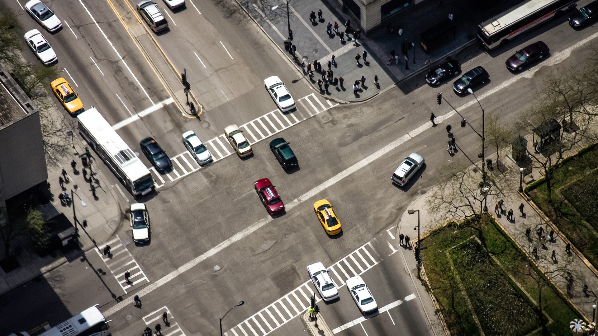 Aerial view of a busy city intersection with cars and pedestrians HD Wallpaper