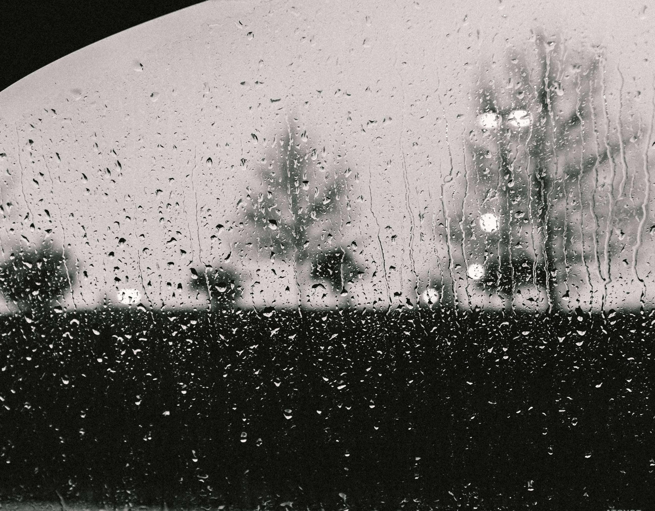 Raindrops on a window with blurred trees and lights HD Wallpaper