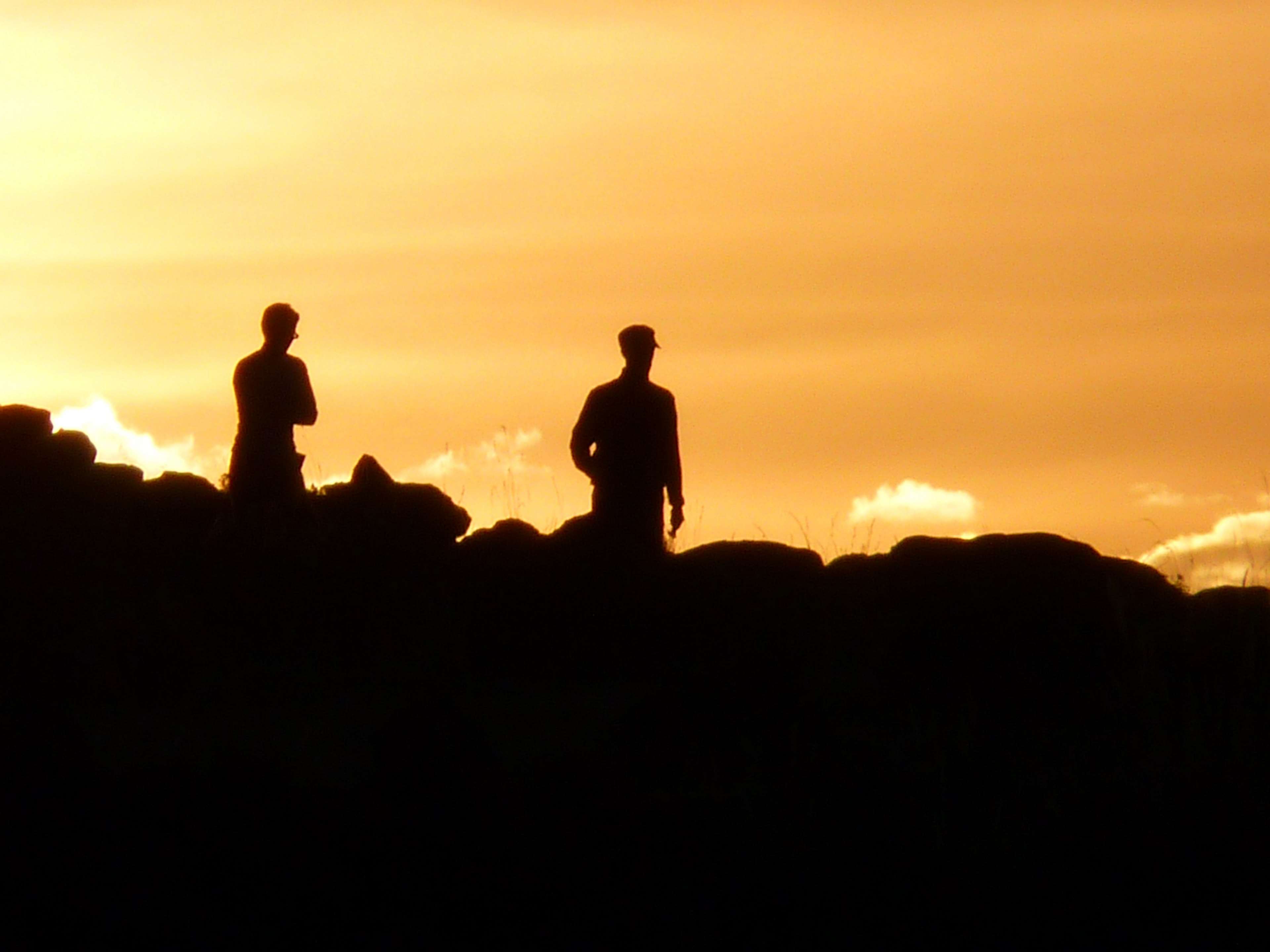 Two men silhouetted against a sunset sky HD Wallpaper