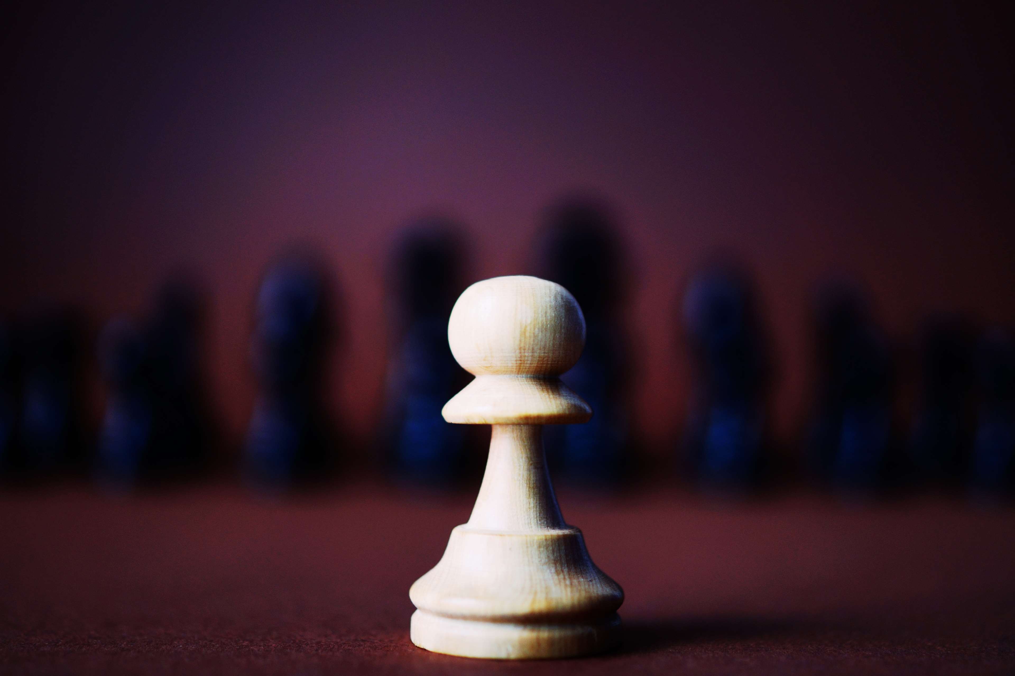 White pawn chess piece in focus, blurred dark pieces behind HD Wallpaper