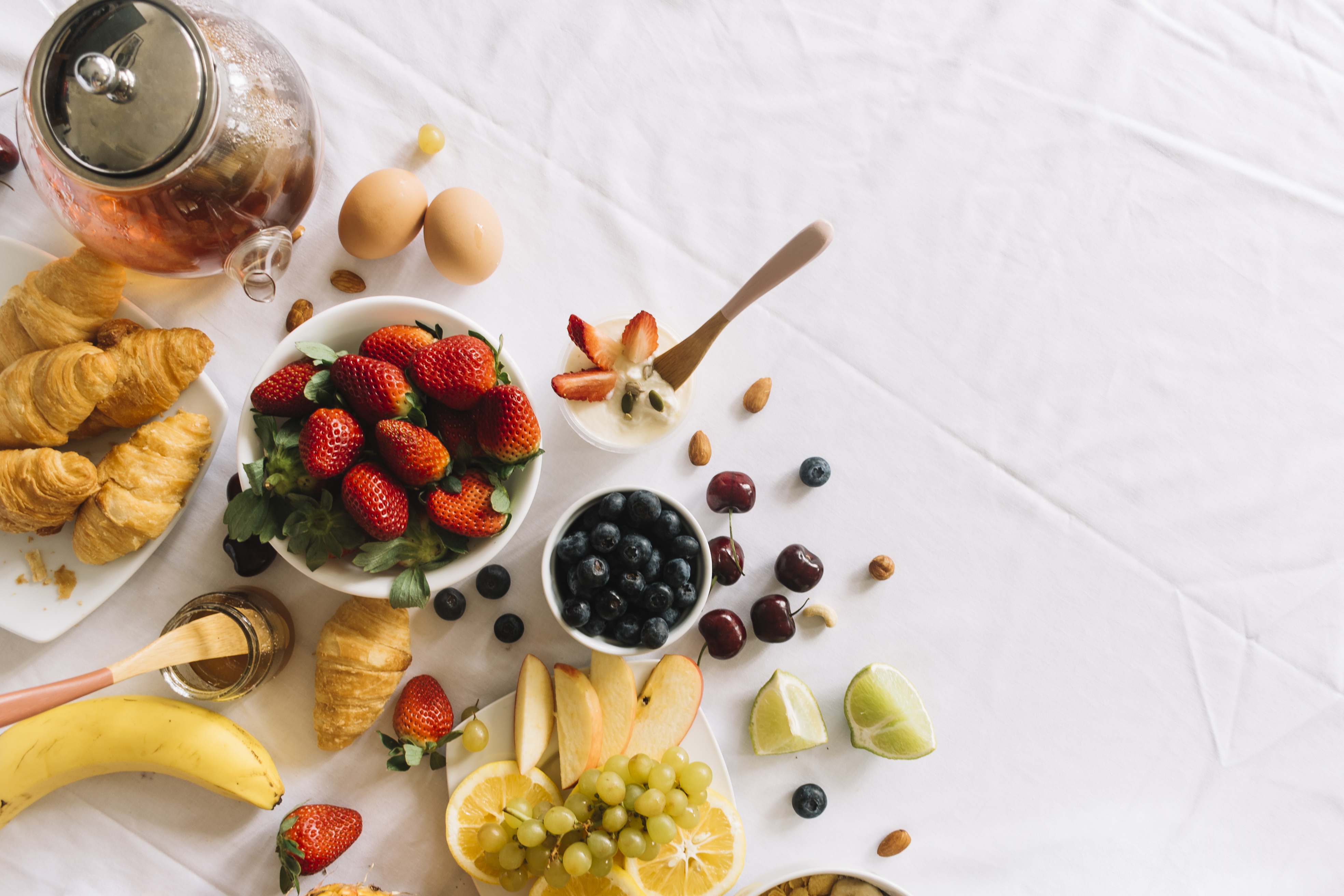 Breakfast spread with croissants, fruits, and tea HD Wallpaper