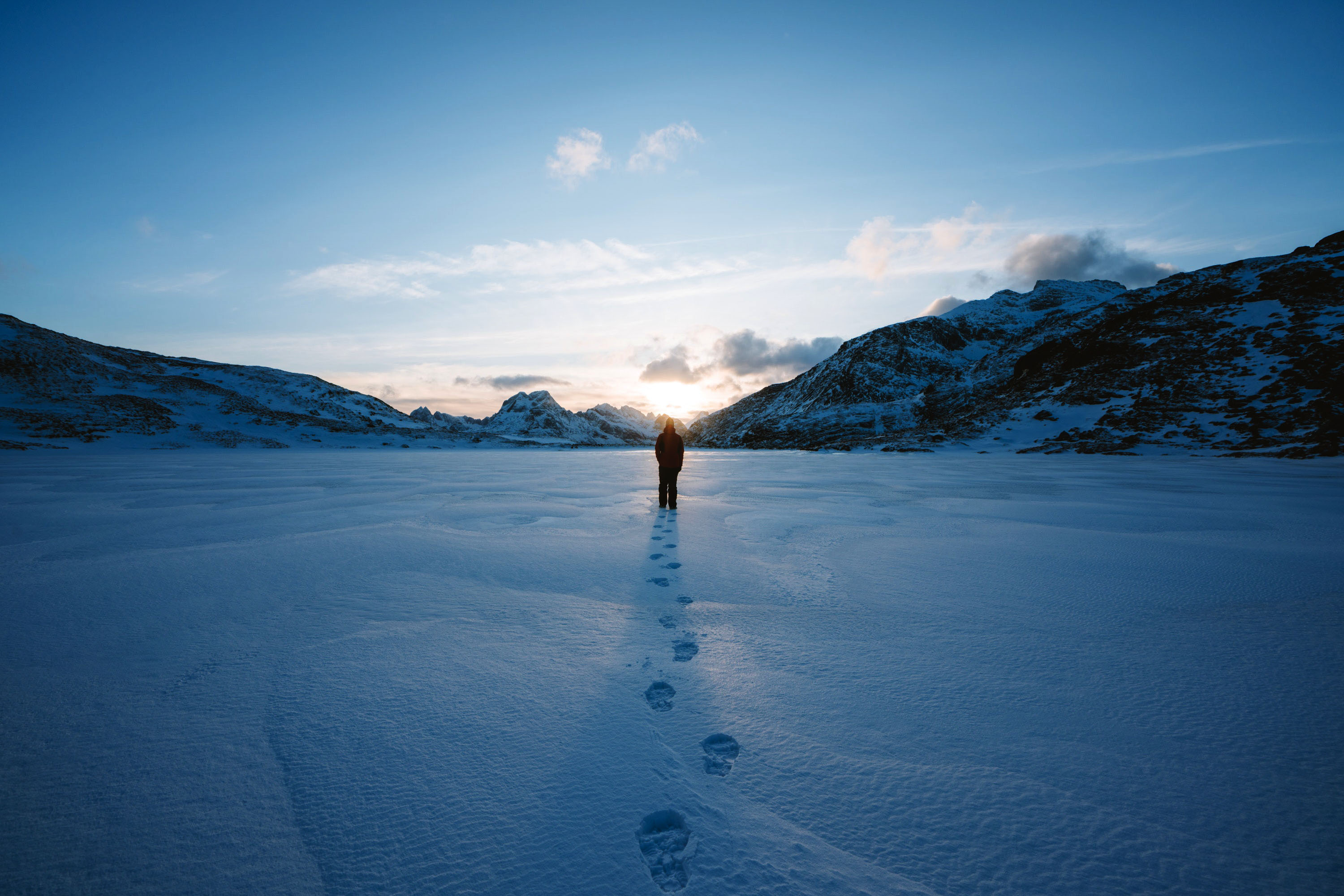 Person walking on snow towards mountains at sunset HD Wallpaper