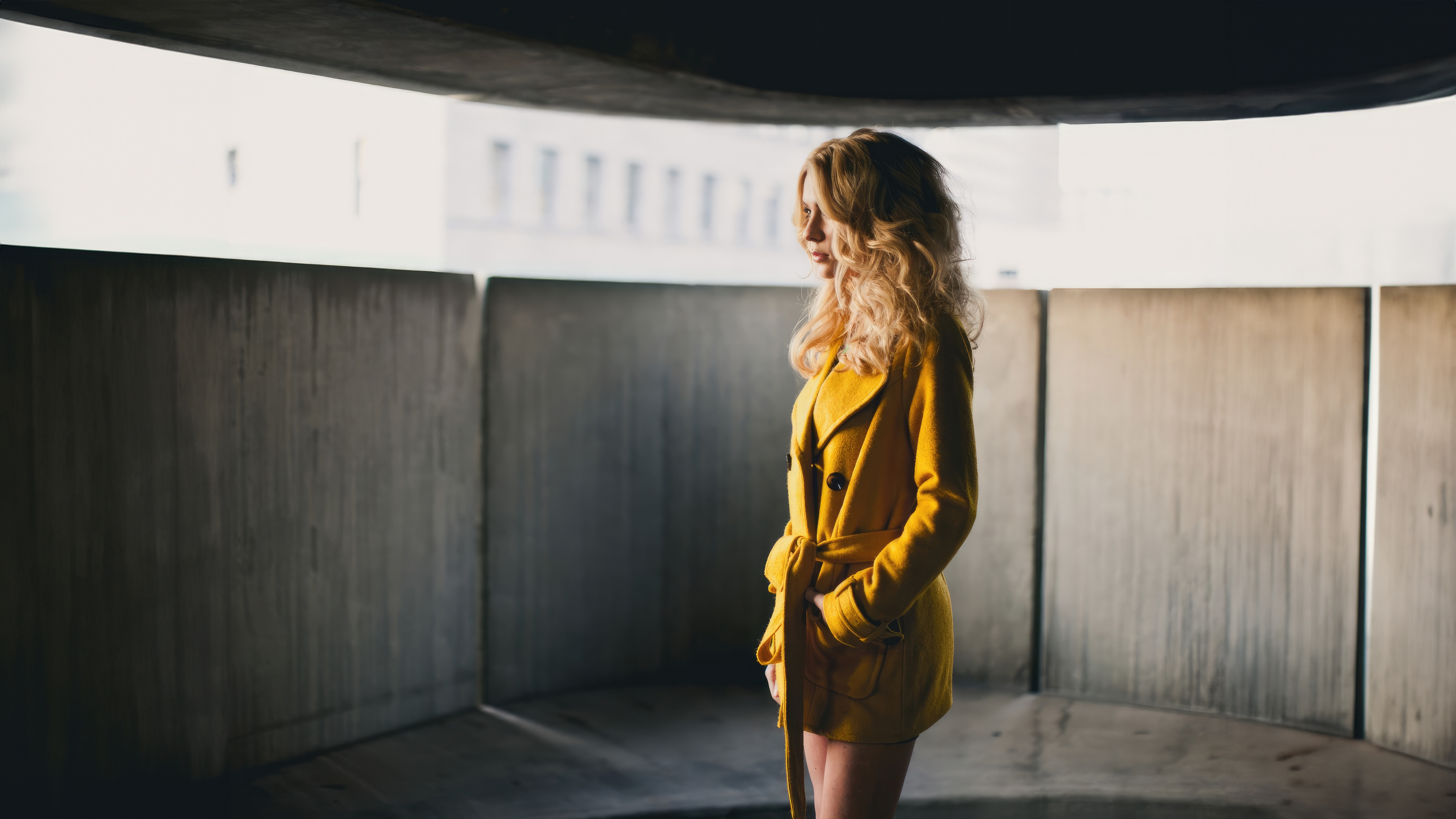 Woman in yellow coat standing in concrete structure HD Wallpaper