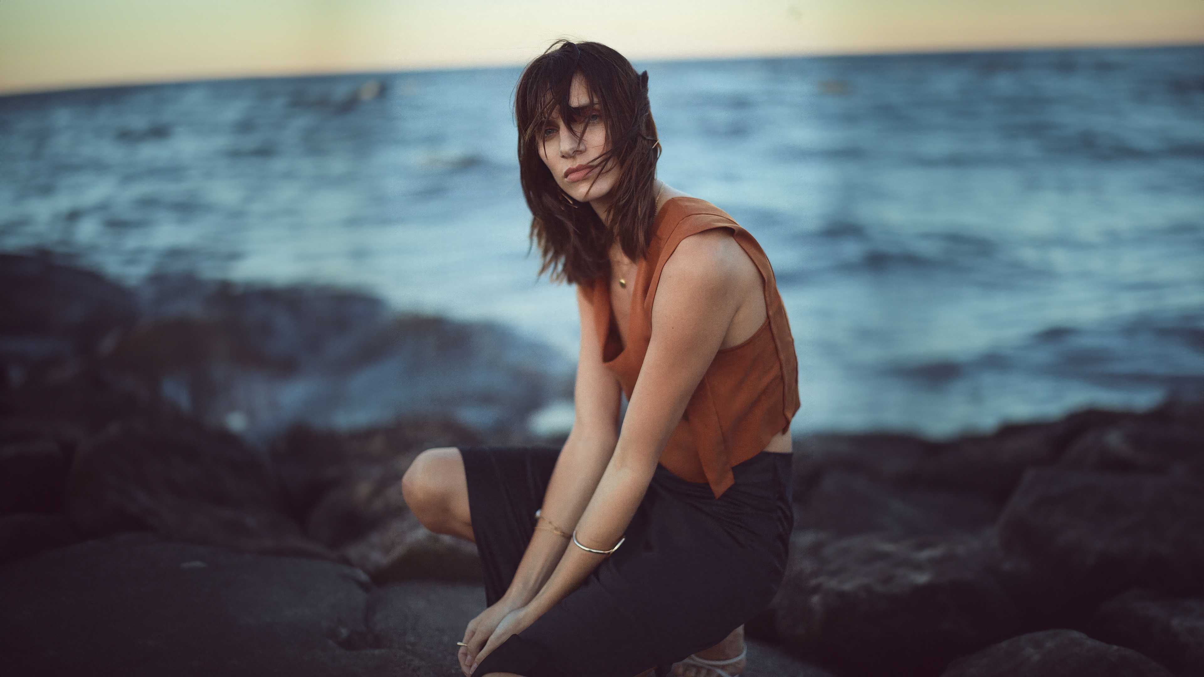 Woman crouching on rocks by the sea HD Wallpaper