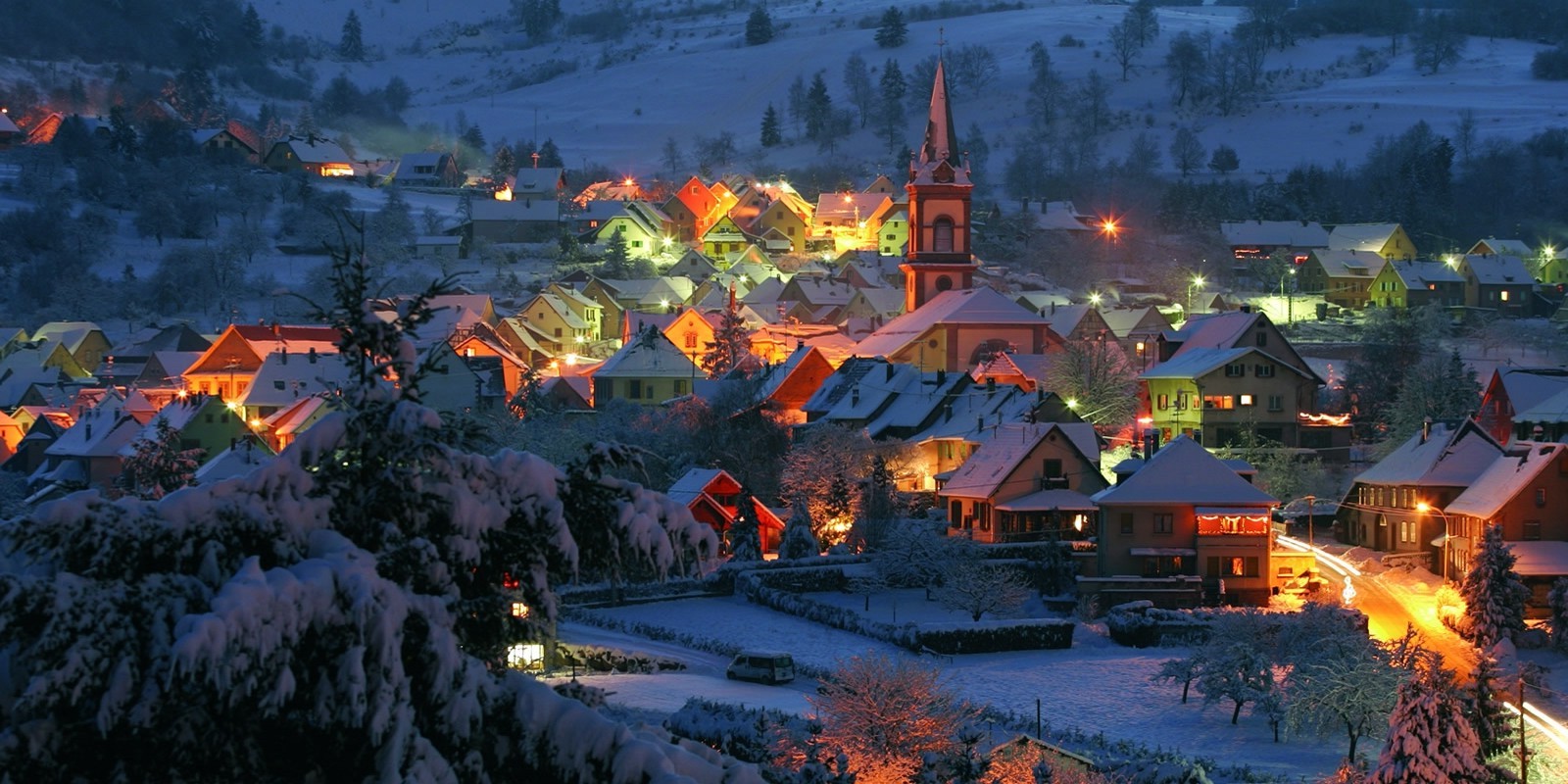 Snowy village at night with illuminated houses and church HD Wallpaper