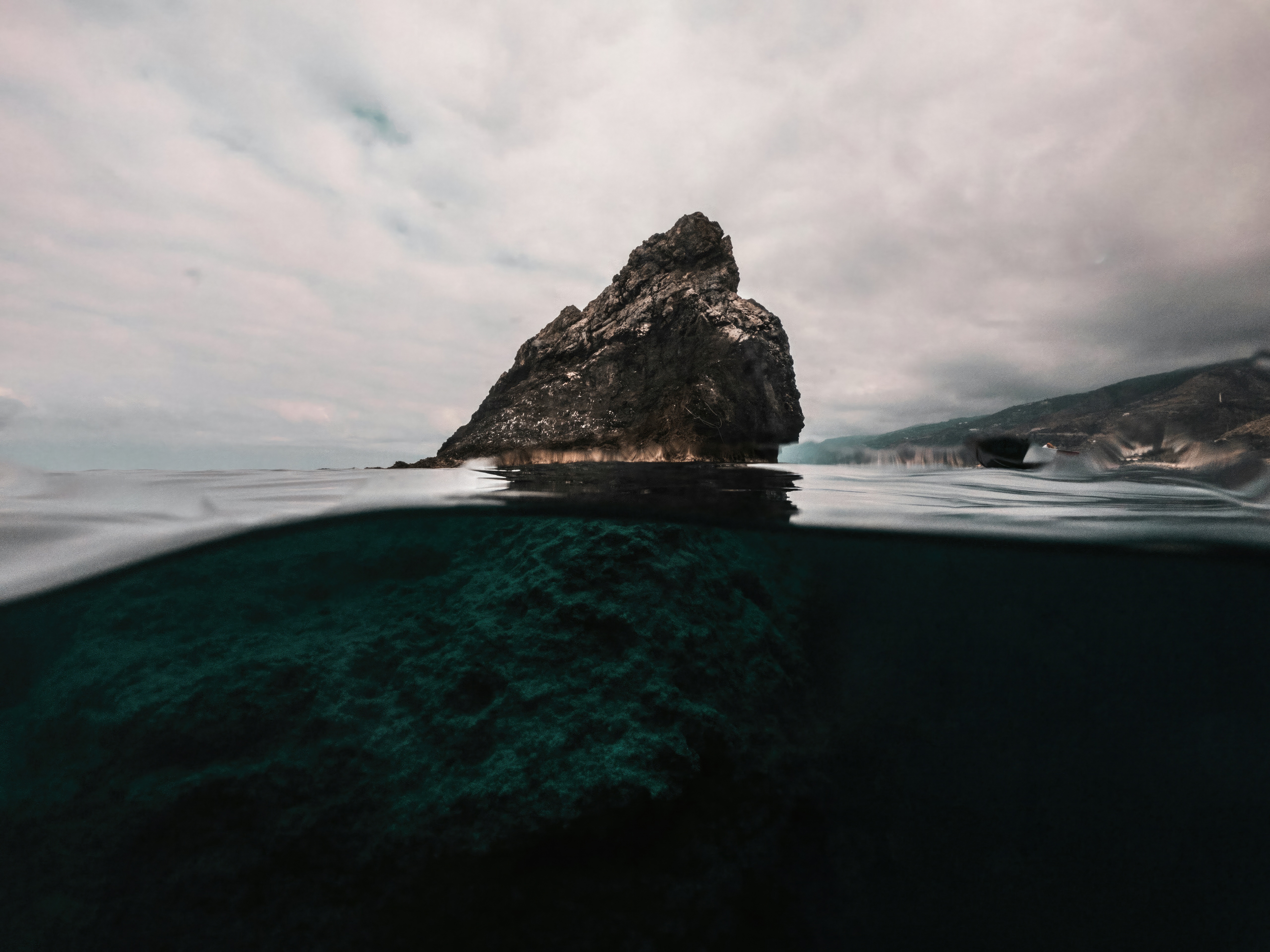 A large rock formation emerges from the ocean HD Wallpaper