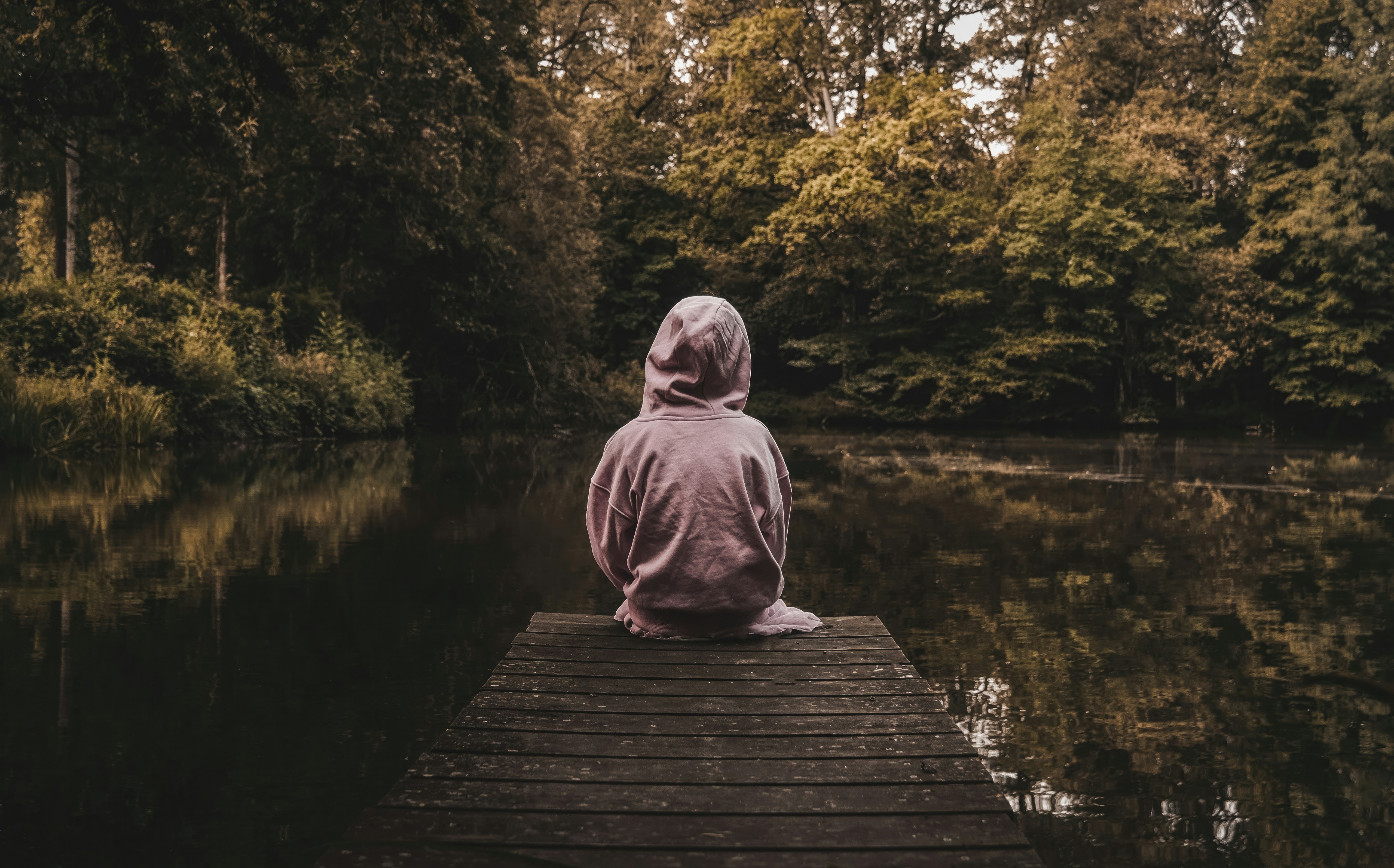 Child sitting on a wooden pier by a lake HD Wallpaper