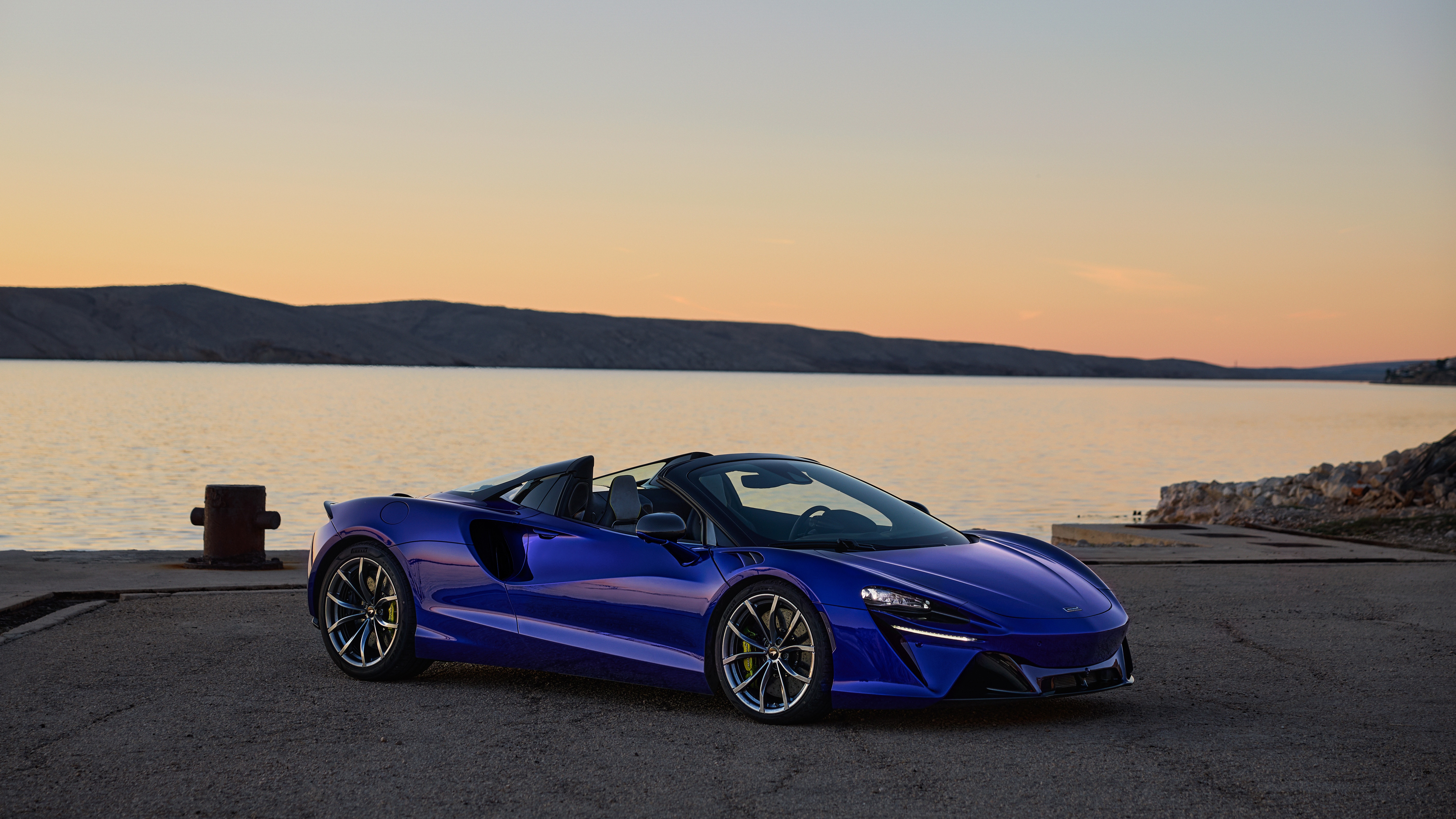 Blue McLaren Artura Spider convertible by the water at sunset HD Wallpaper