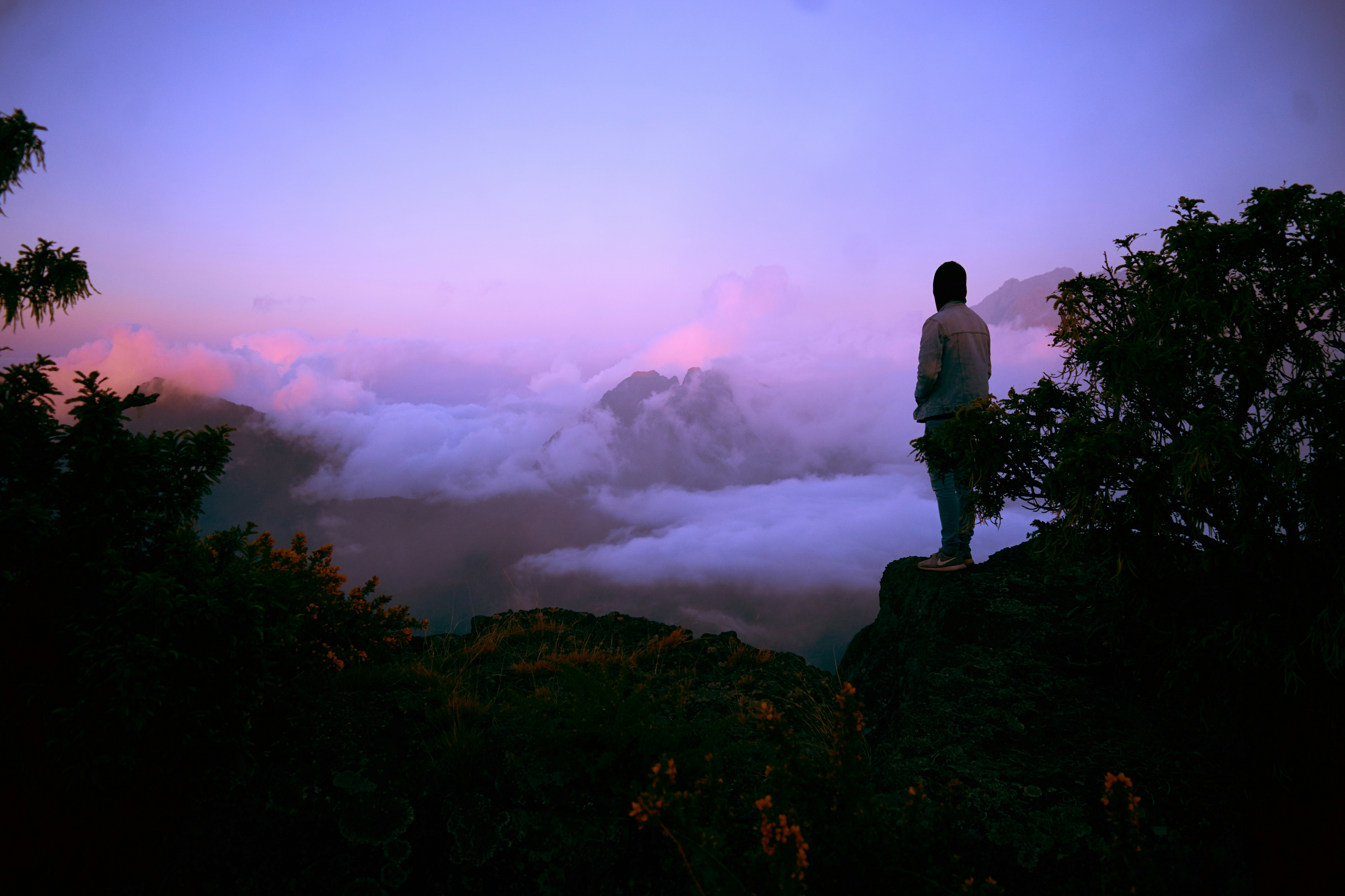 Man on cliff overlooking clouds at sunset HD Wallpaper