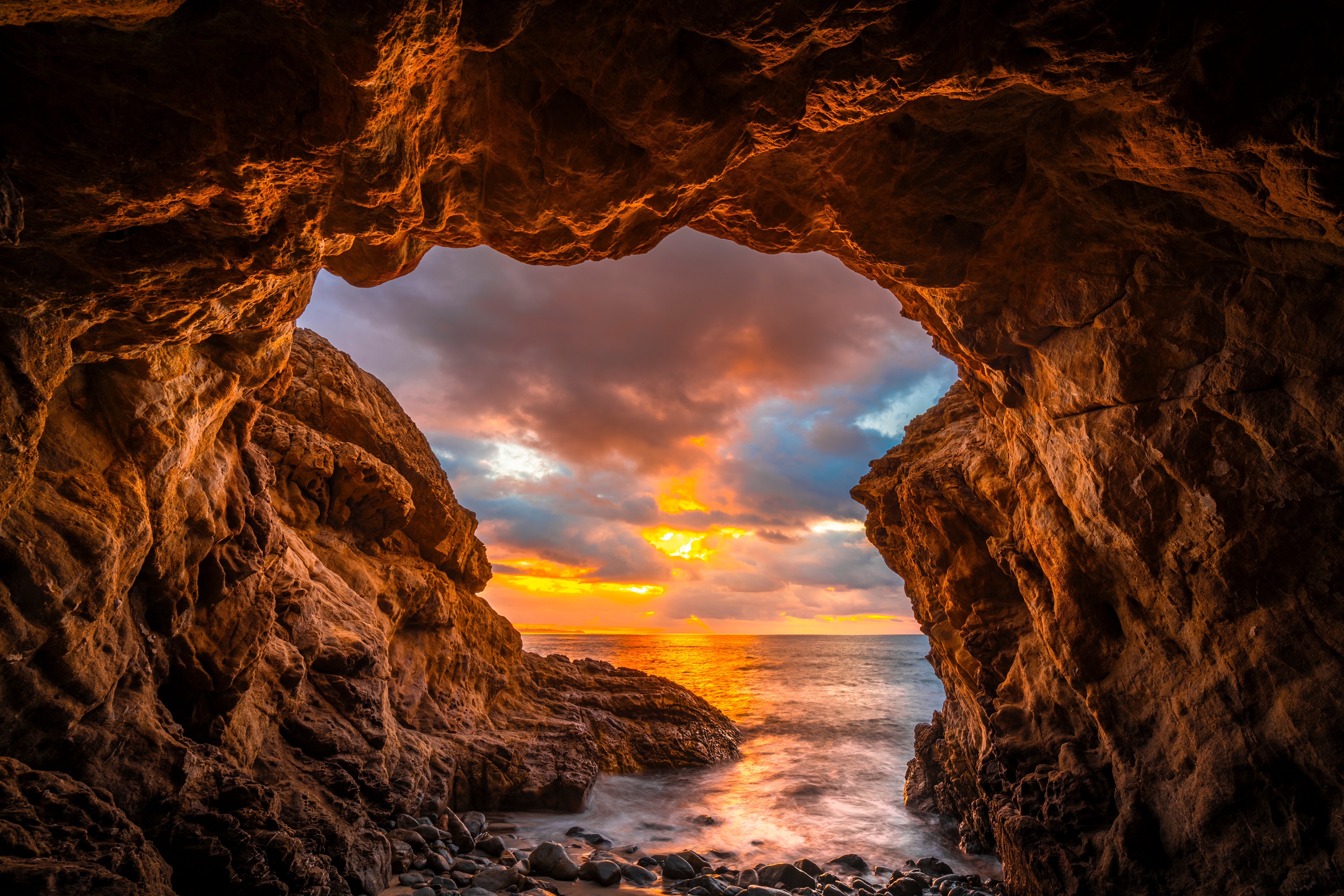 Cave entrance overlooking a sunset over the ocean HD Wallpaper