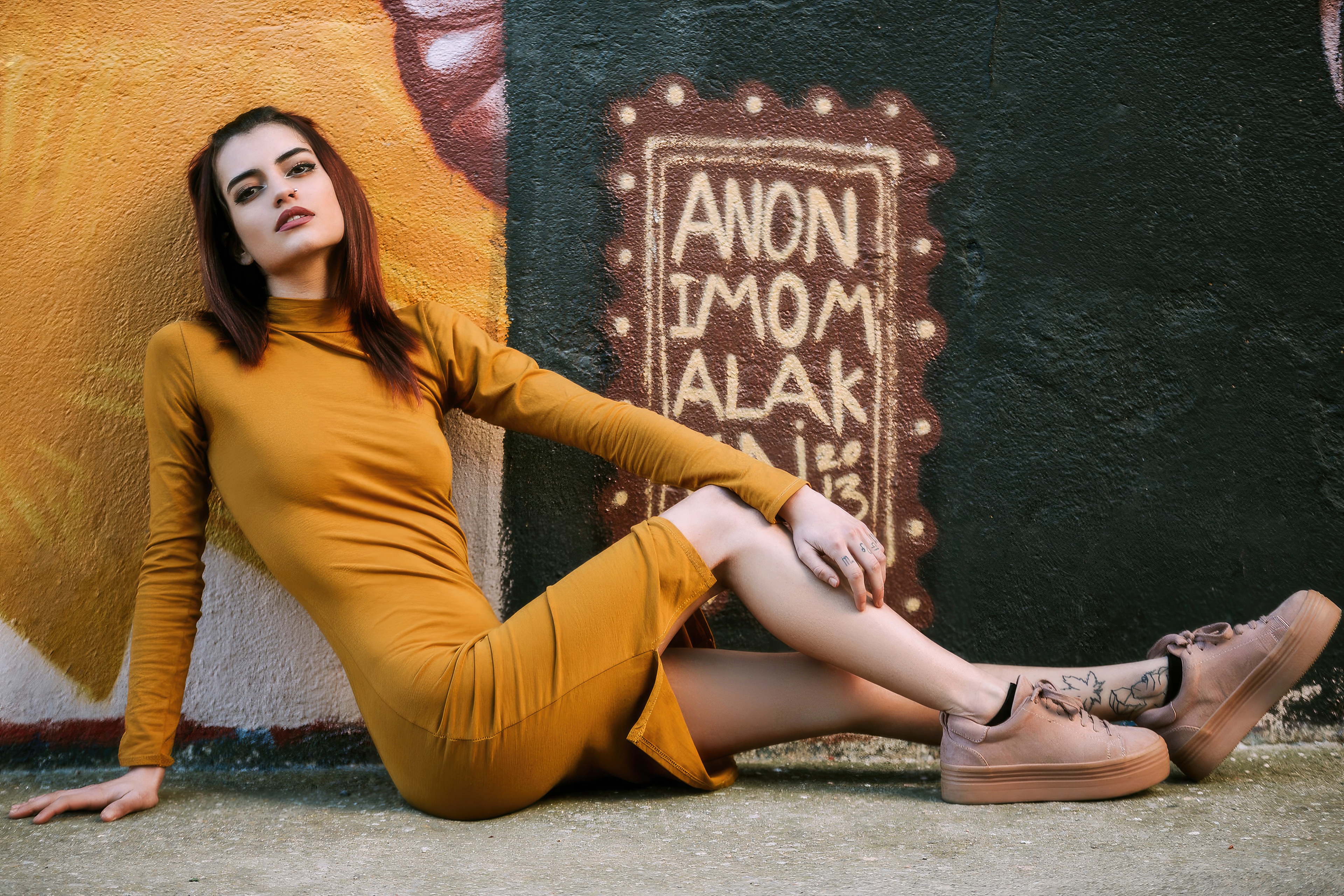 Girl in a mustard dress sitting by a graffiti wall HD Wallpaper