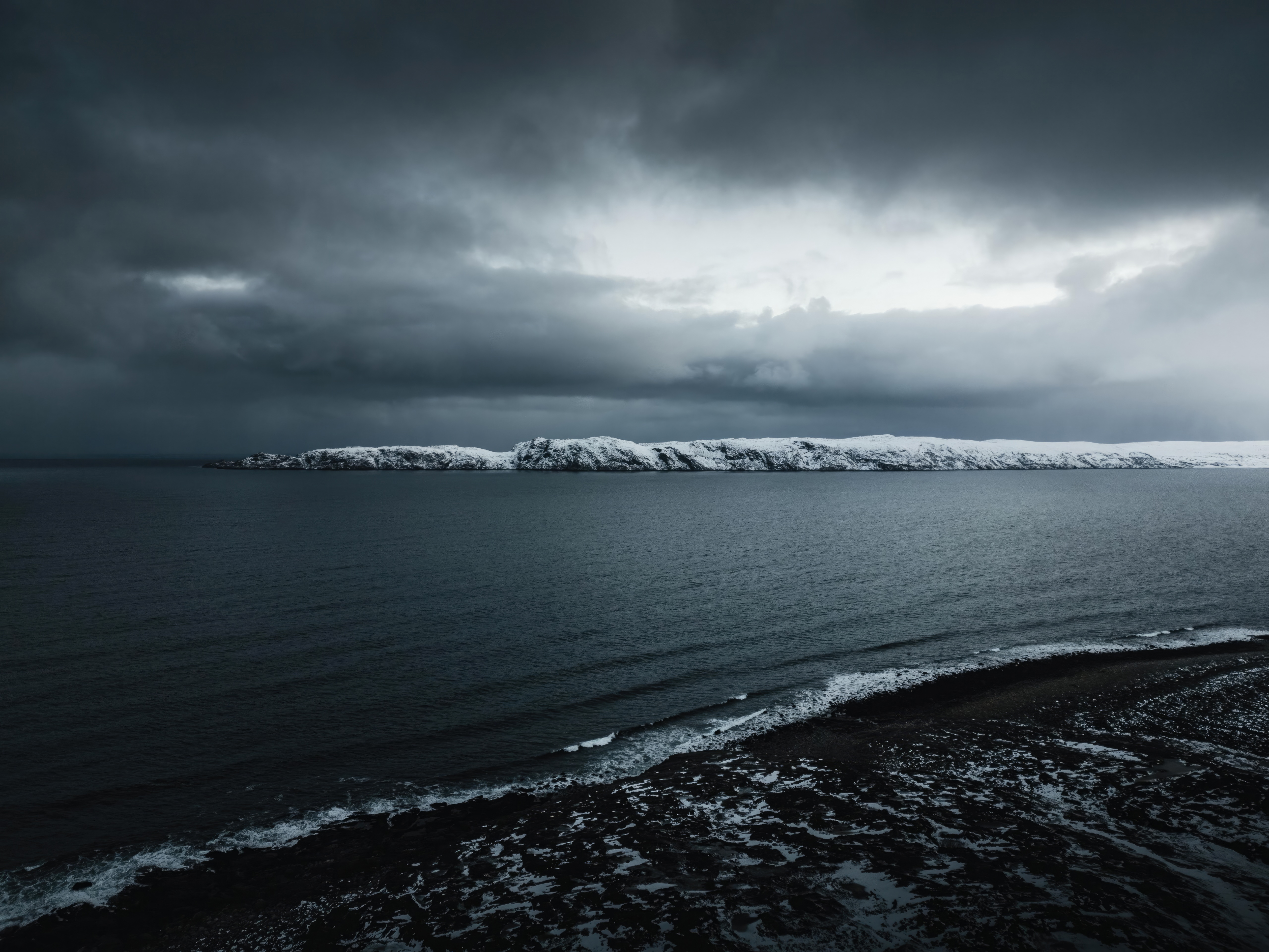 Dark Ocean and Snow-Covered Island Under Stormy Sky HD Wallpaper