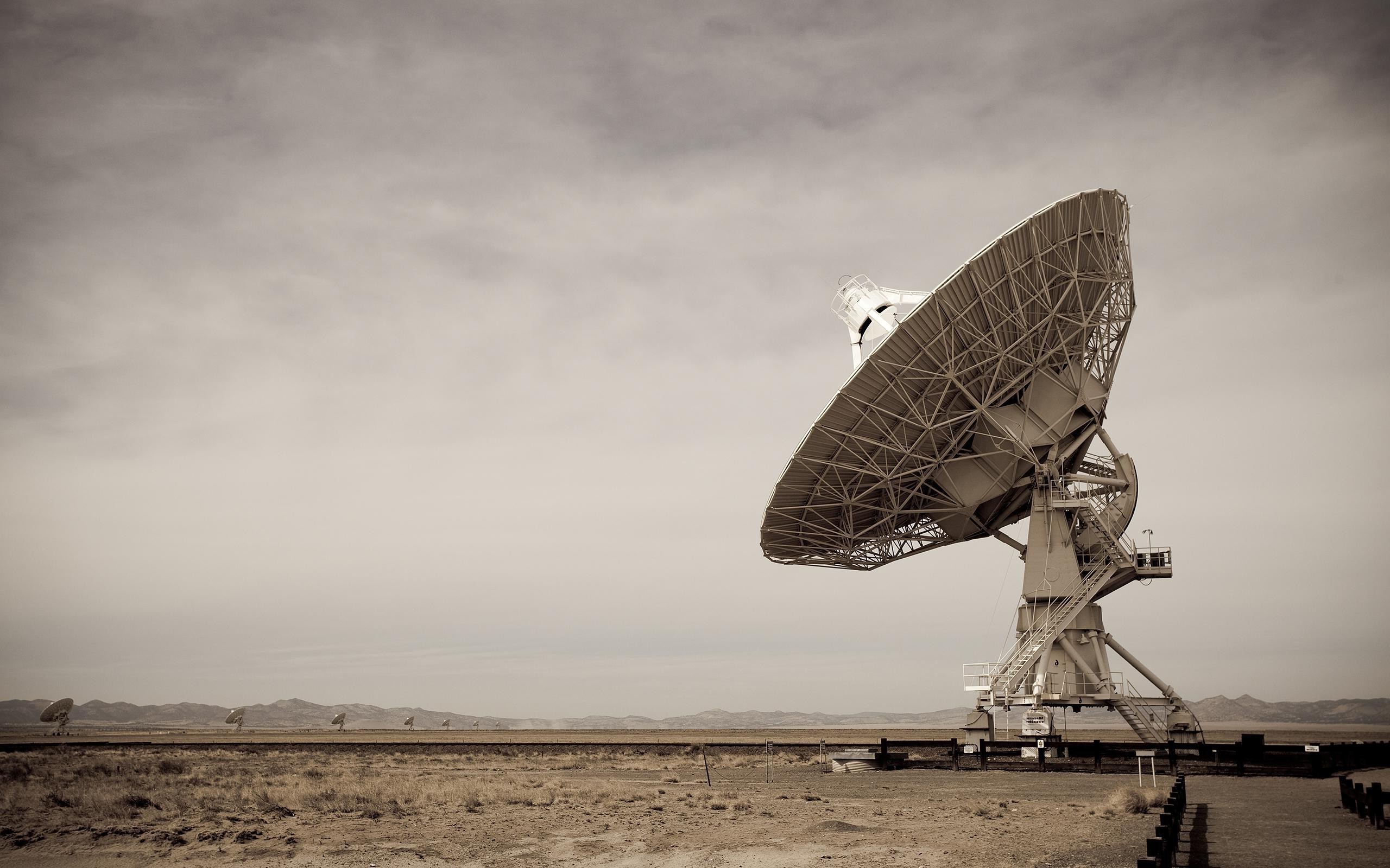 Satellite dishes in a desert landscape under a cloudy sky HD Wallpaper