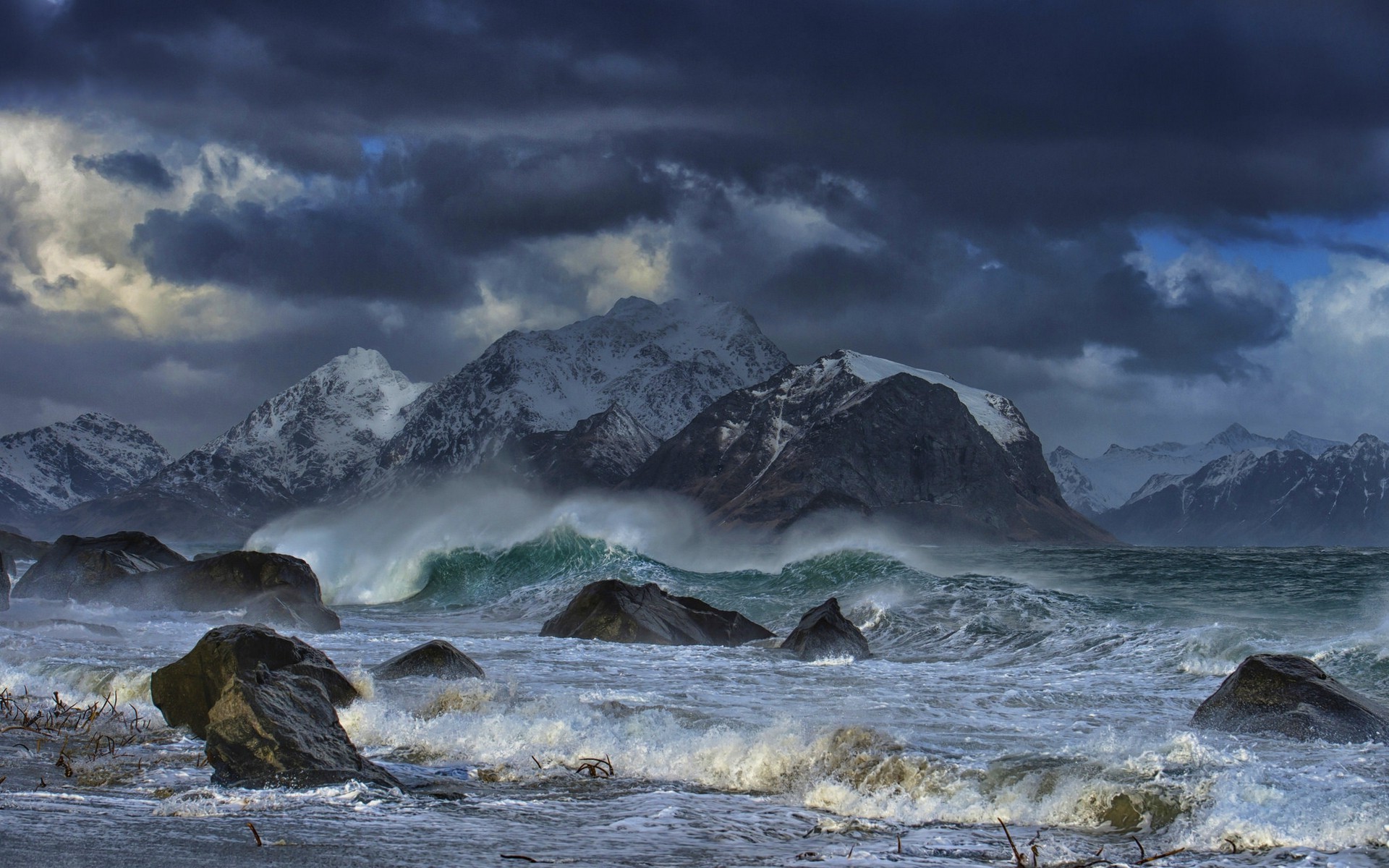 Stormy sea with waves crashing against rocks and snowy mountains HD Wallpaper