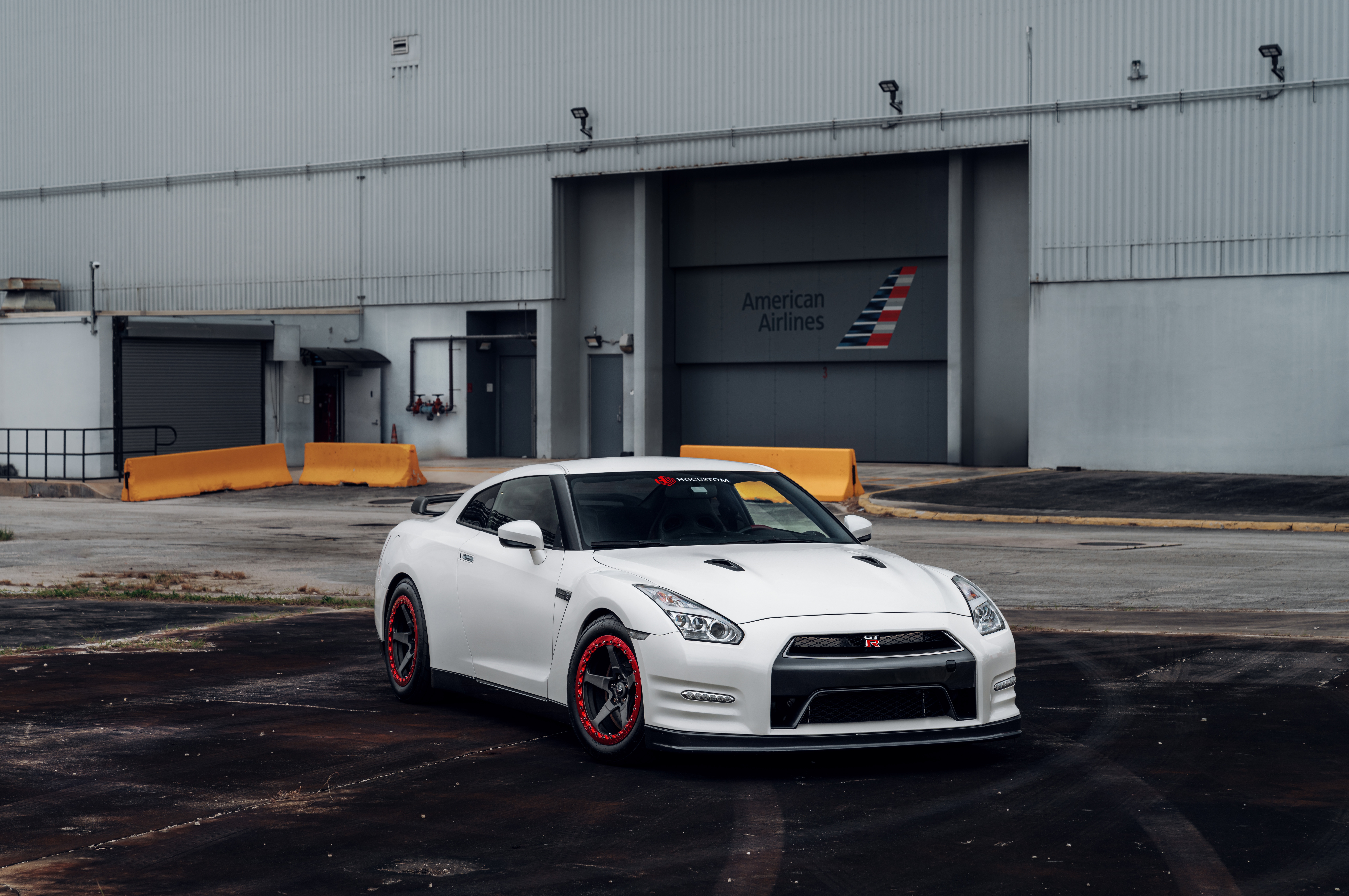 White Nissan GTR parked in front of American Airlines hangar HD Wallpaper