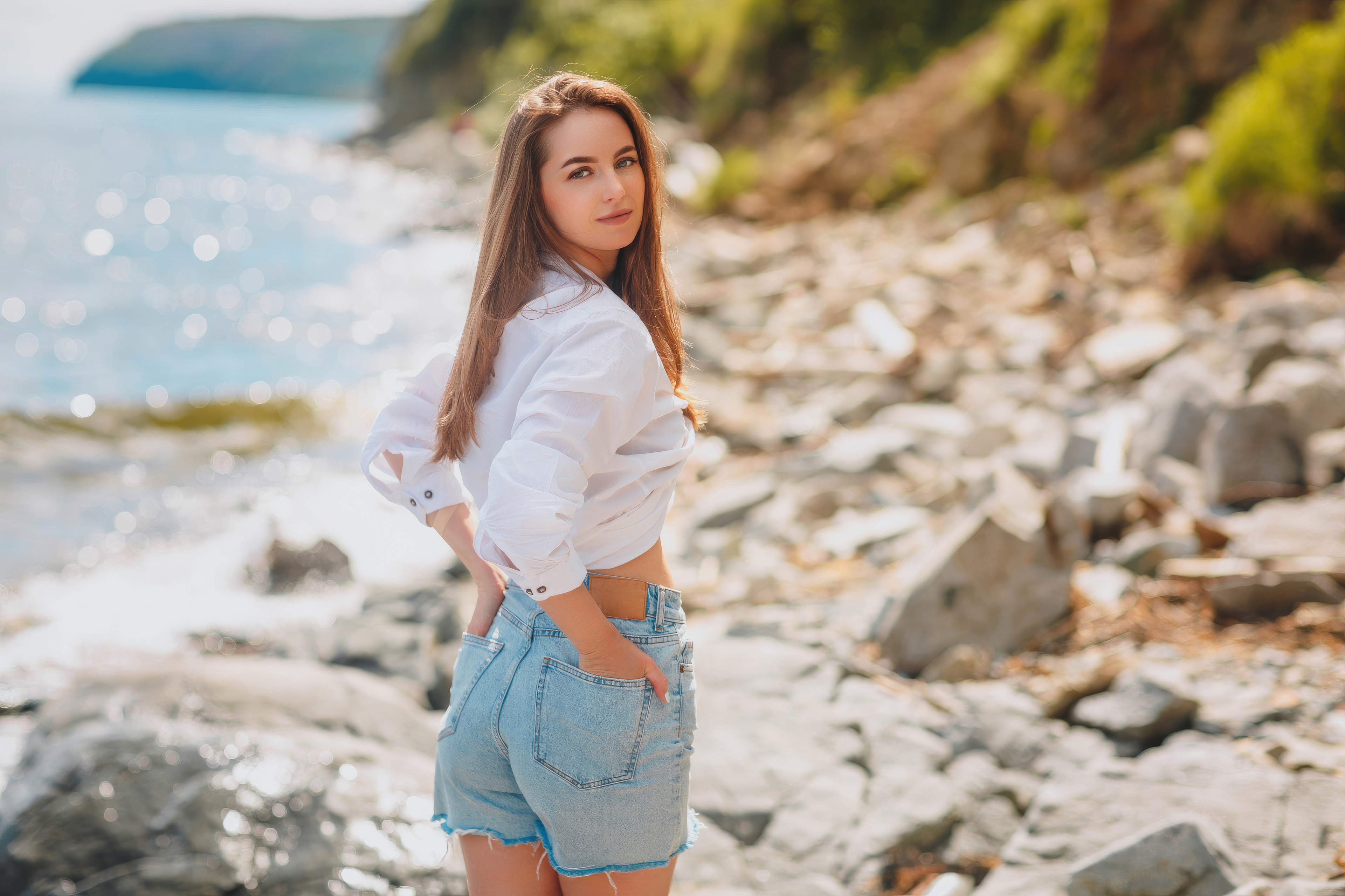 Girl with hands in back pocket on a rocky beach HD Wallpaper