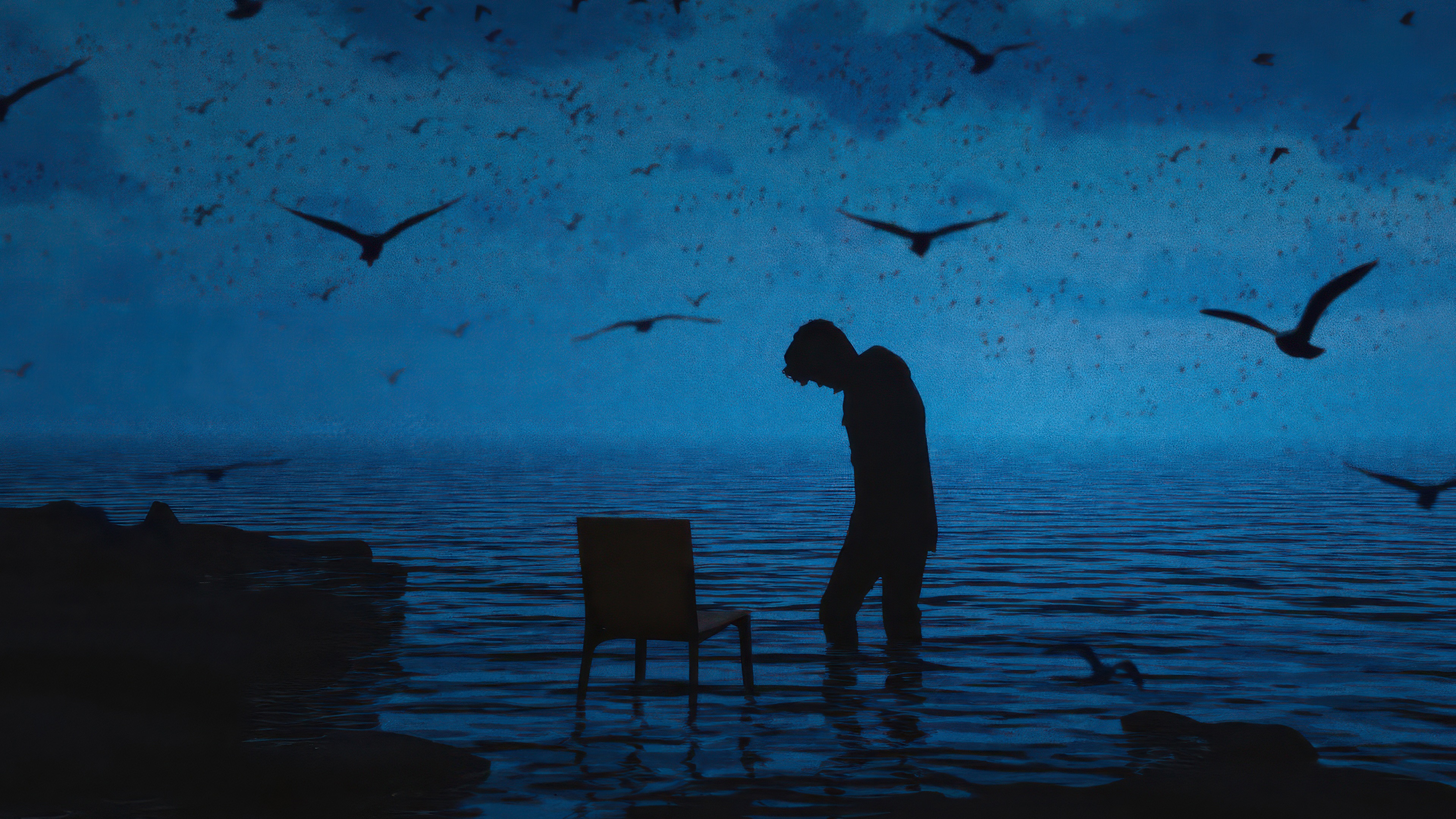 Silhouette of a man standing in water with a chair HD Wallpaper