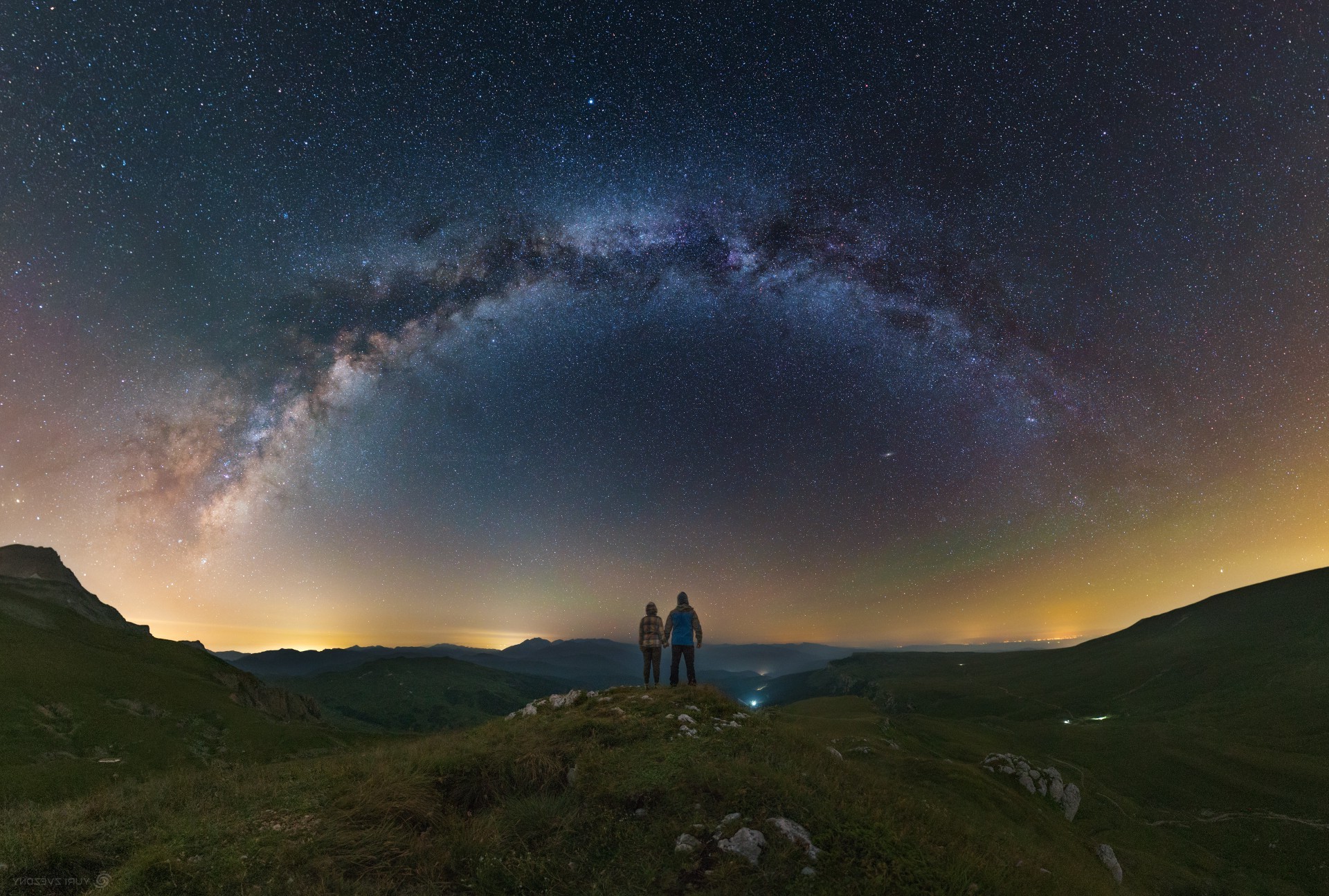 Two people looking at the Milky Way over mountains at night HD Wallpaper