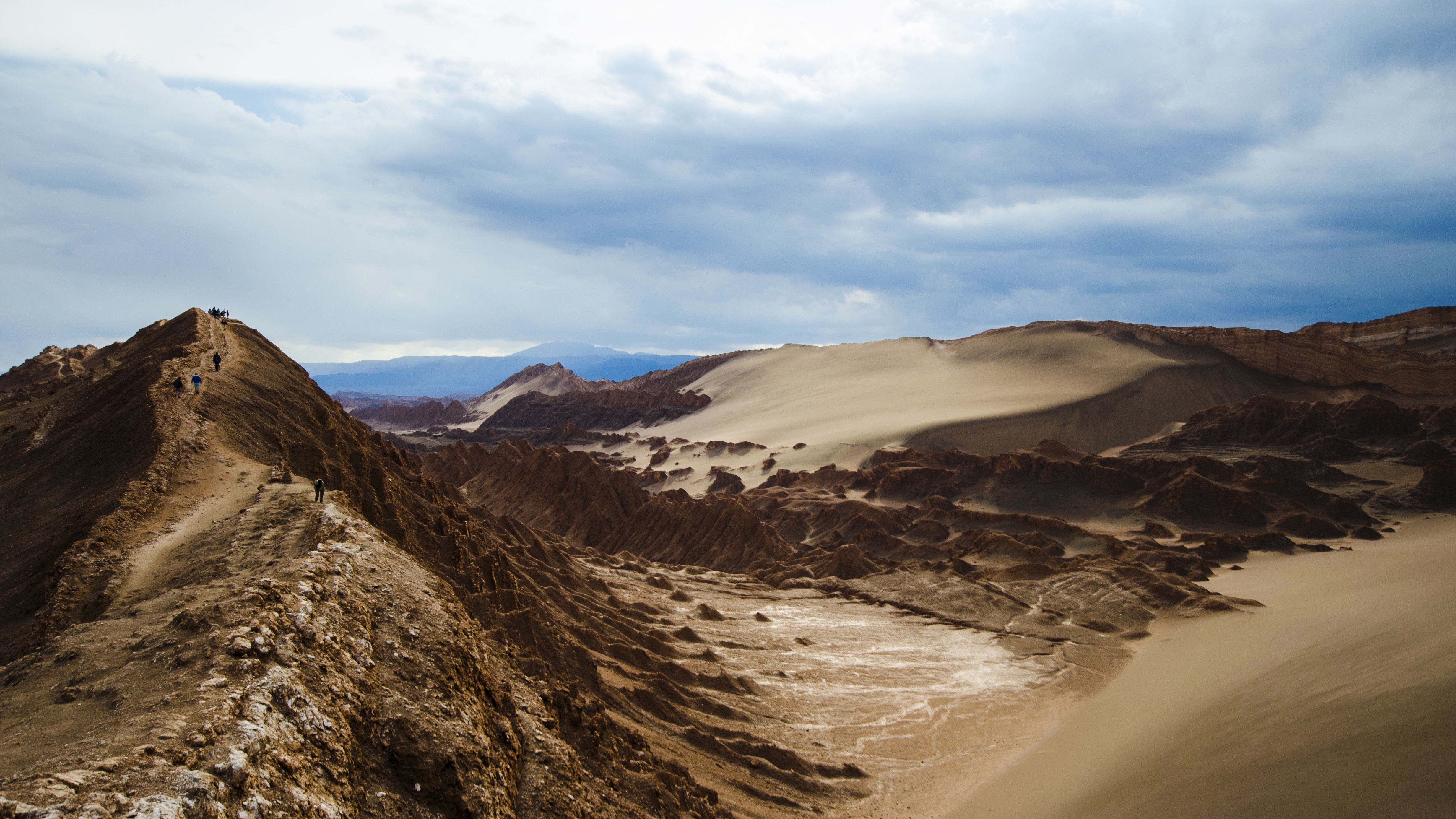 People hiking on a mountain ridge in a desert landscape HD Wallpaper
