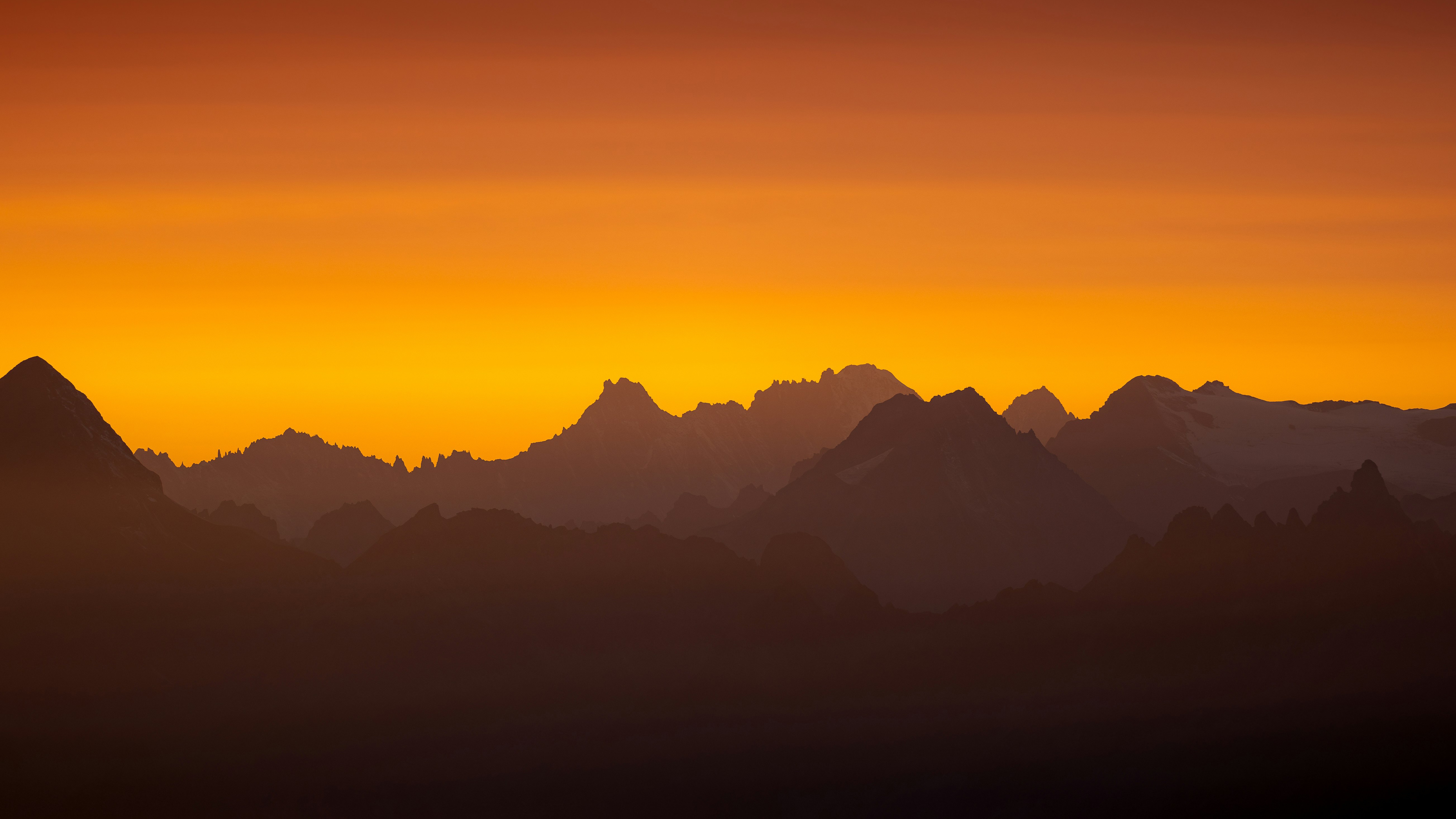 Sunset over a silhouetted mountain range HD Wallpaper