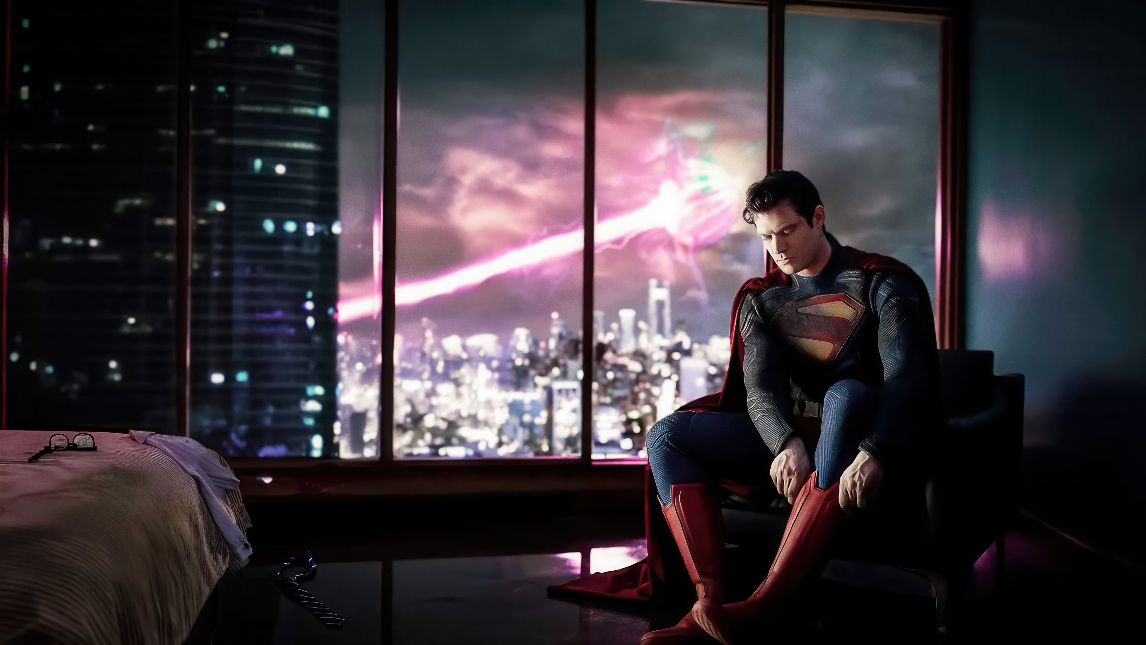 Superman putting on his boots in a room overlooking a city HD Wallpaper