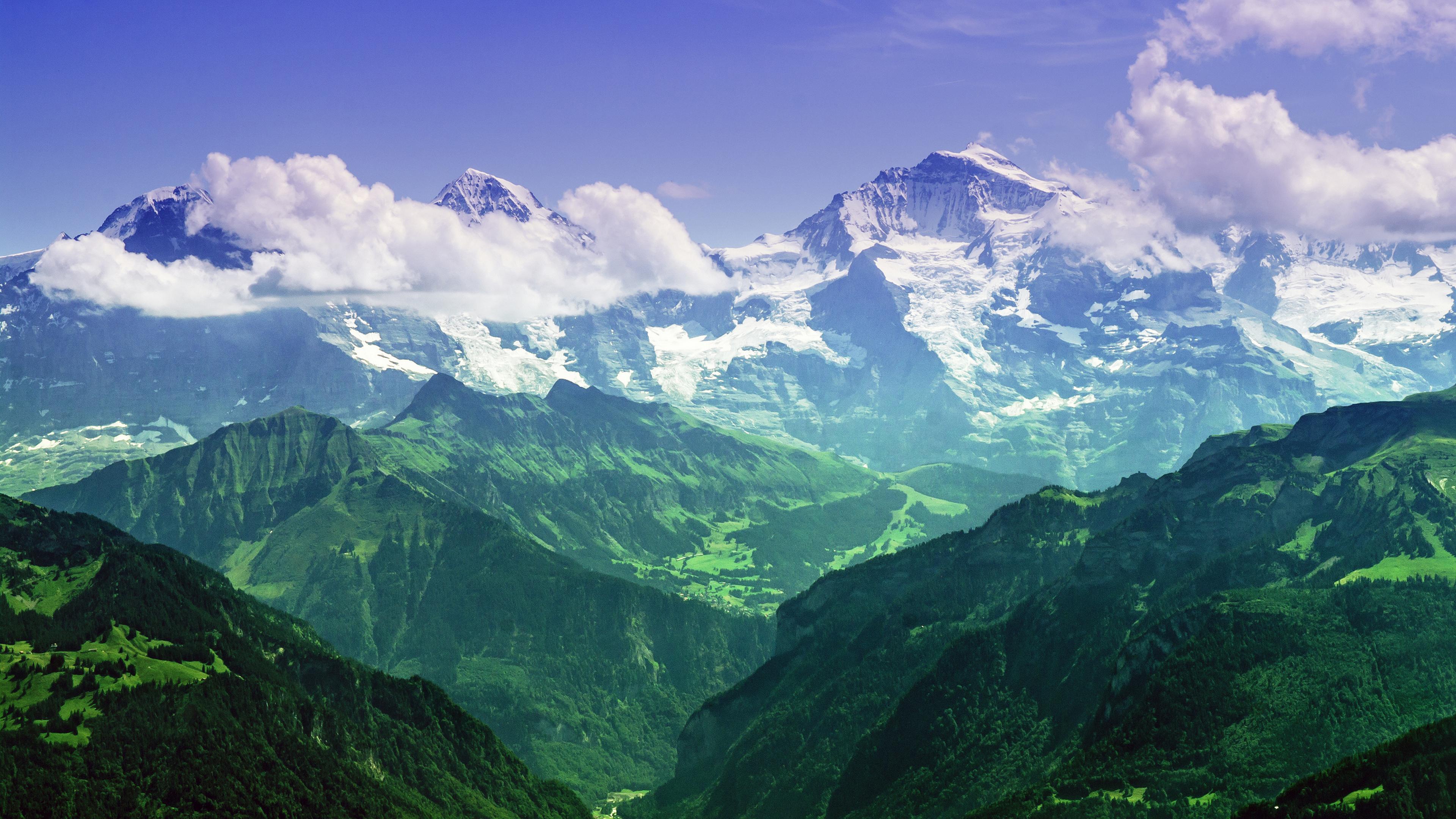 Snow-capped mountains overlooking green valleys HD Wallpaper