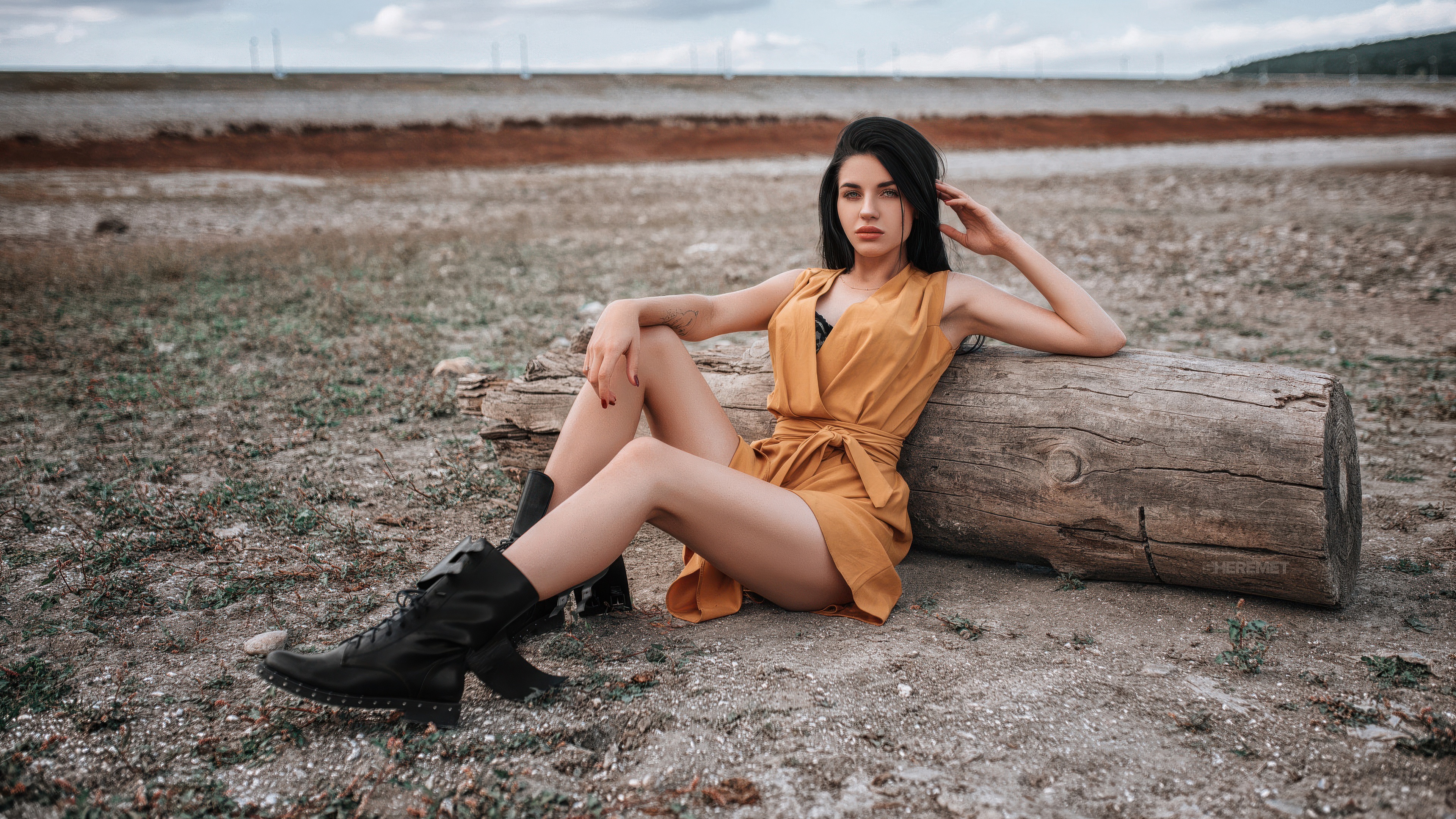 Woman in yellow dress sitting on a log outdoors HD Wallpaper