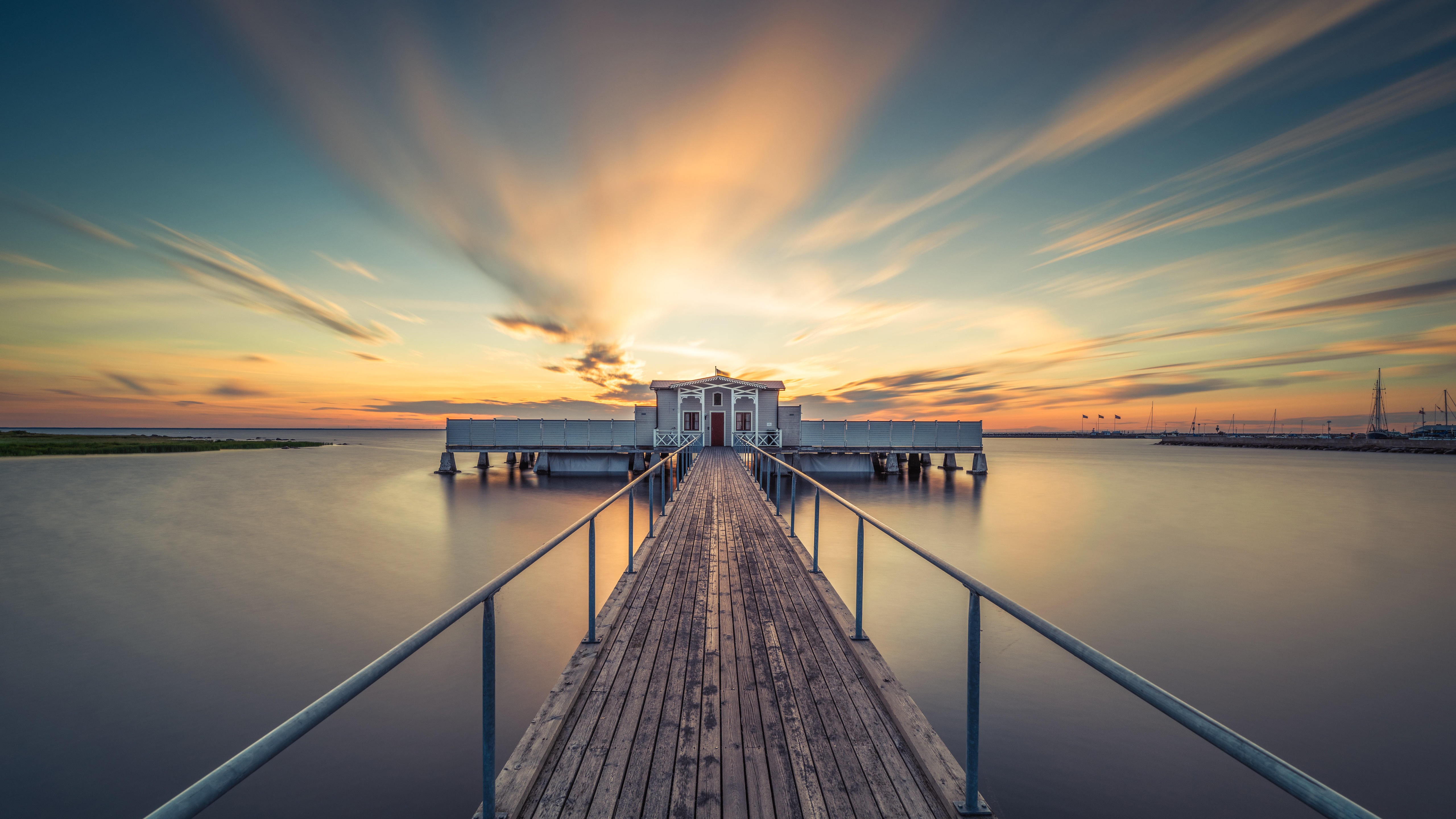 Wooden pier leading to a building over water at sunset HD Wallpaper