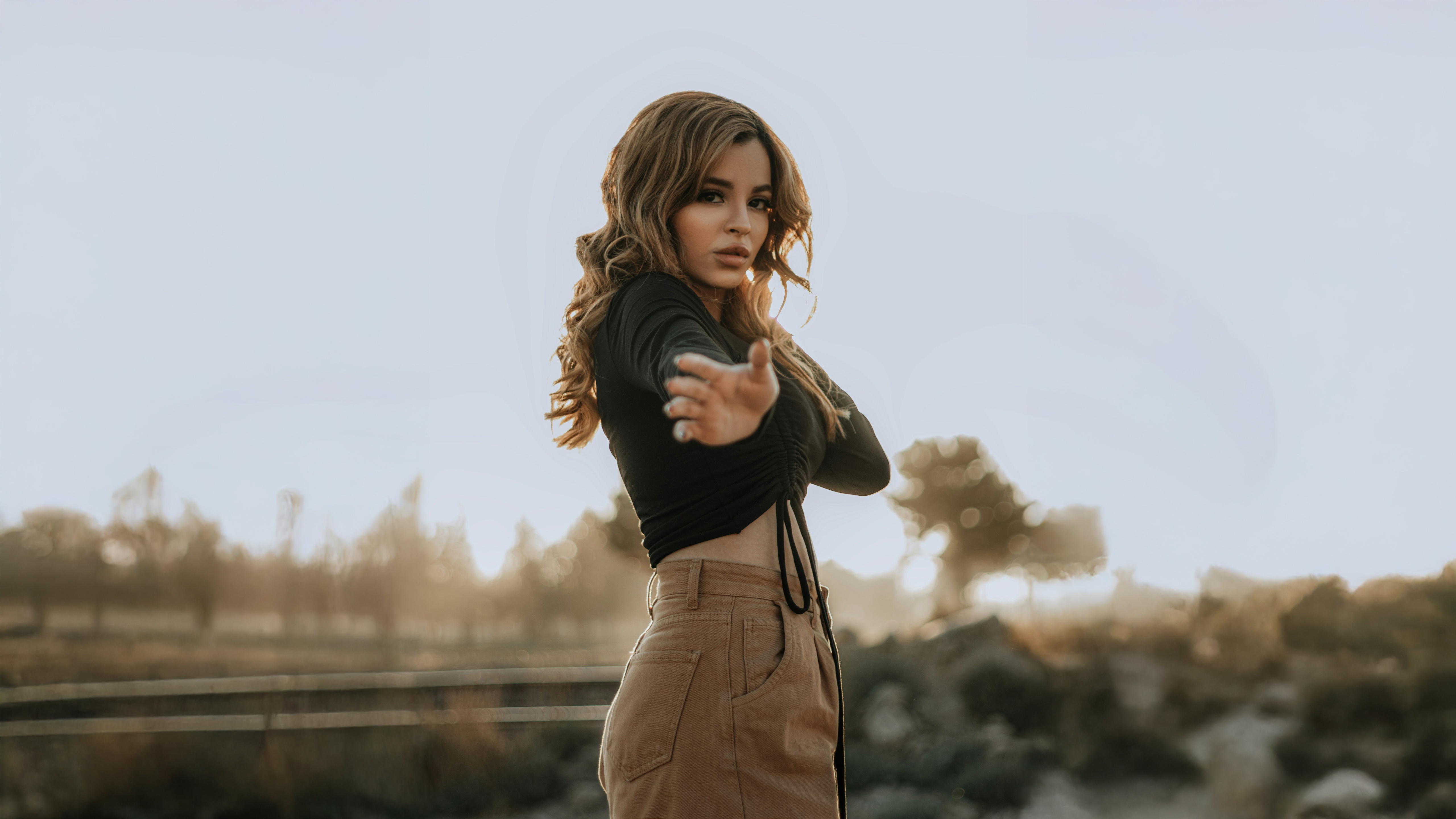 Girl in black top and tan pants posing outdoors HD Wallpaper