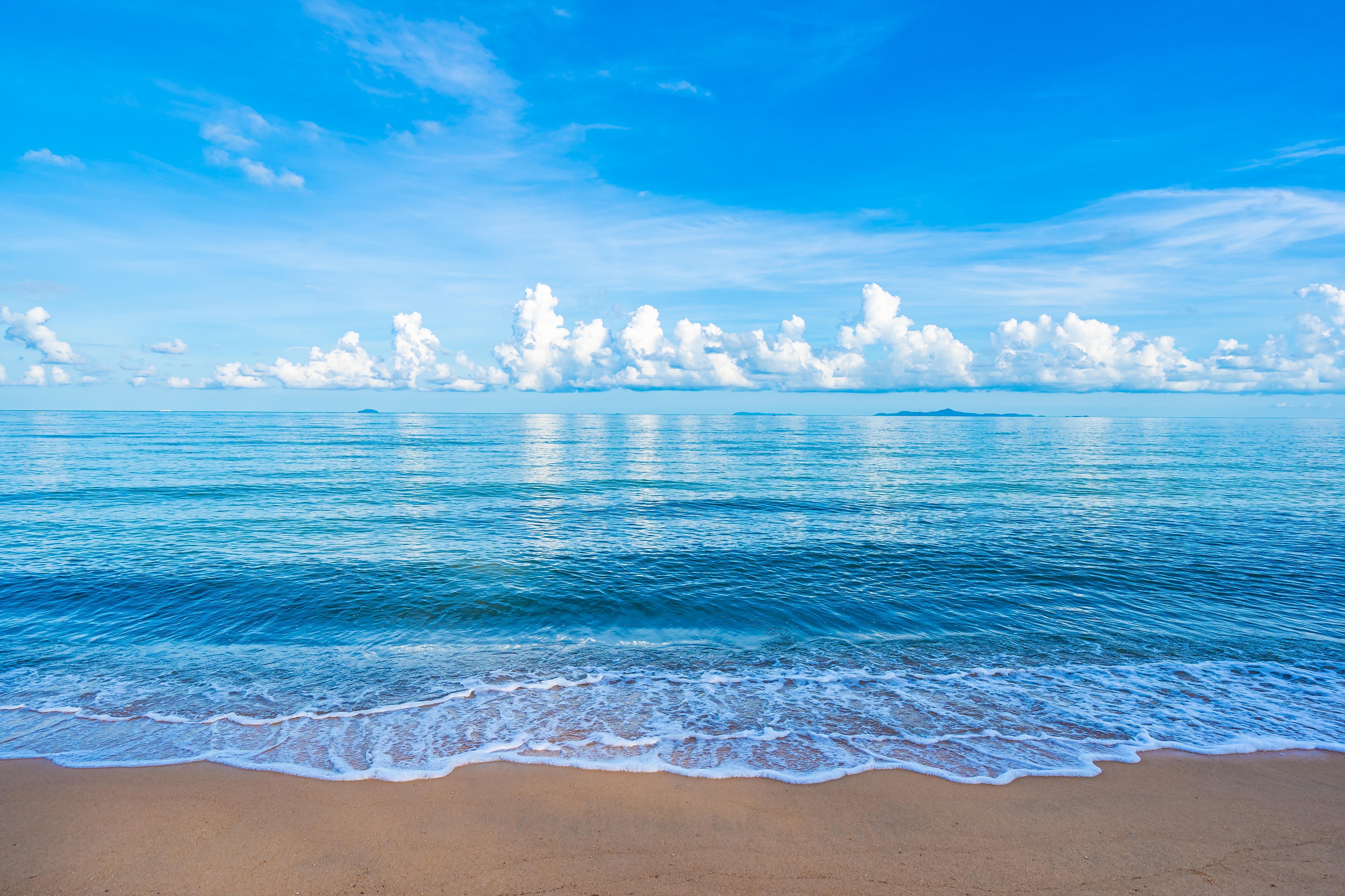 Ocean waves on a sandy beach under a blue sky with clouds HD Wallpaper