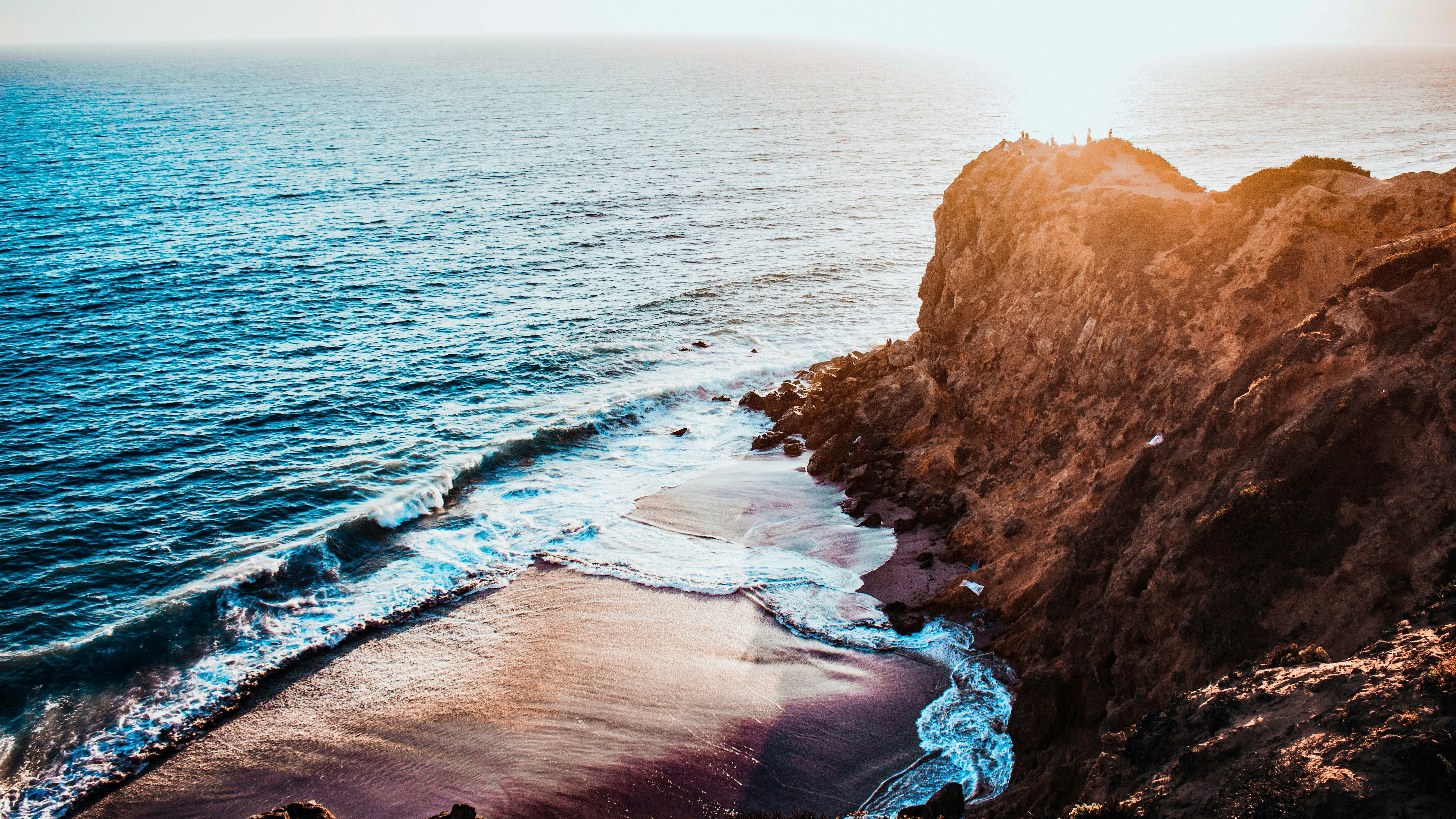 Ocean waves crash on a rocky cliffside in Malibu, California. HD Wallpaper
