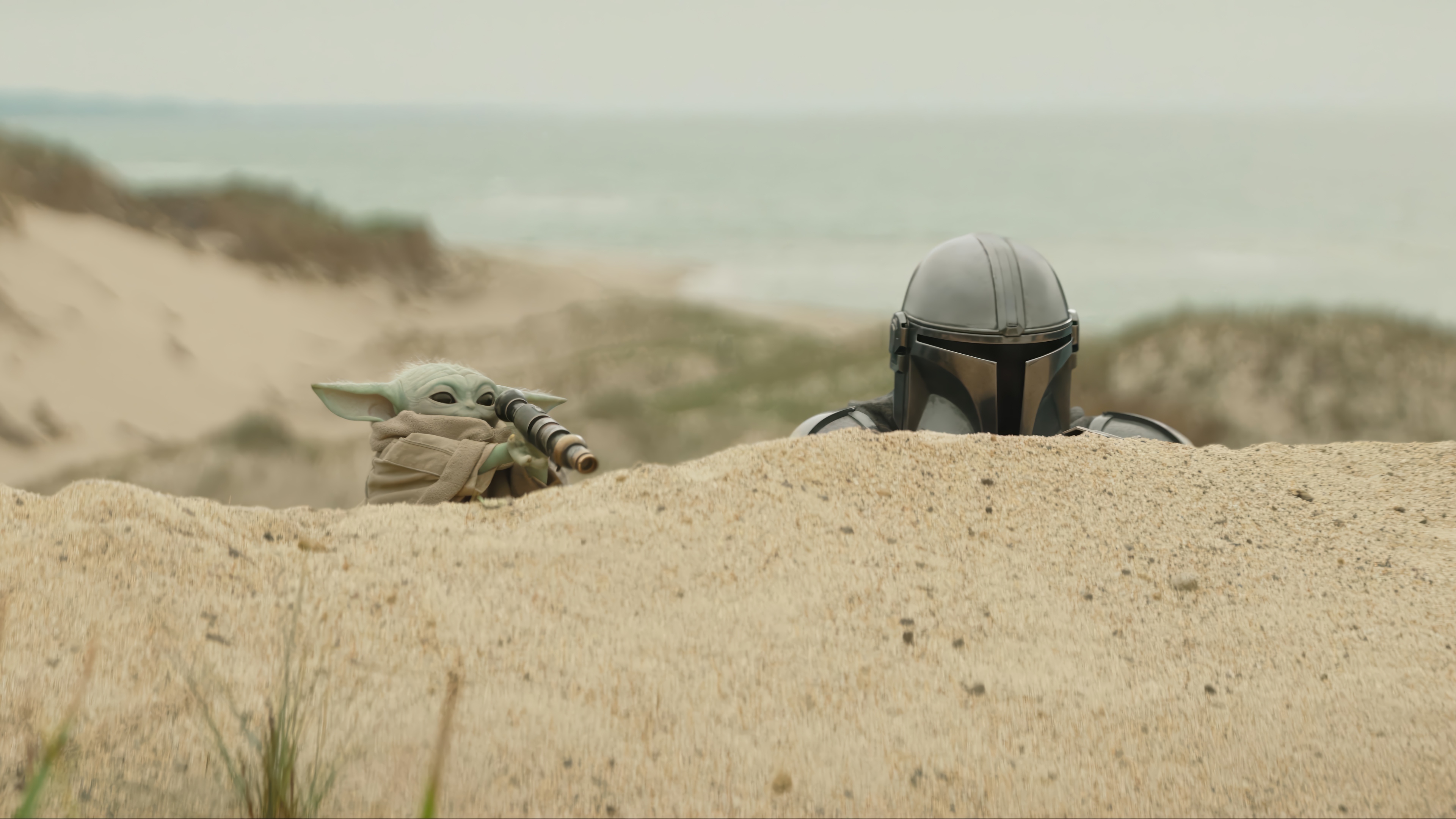 The Mandalorian and Grogu on a sandy beach HD Wallpaper