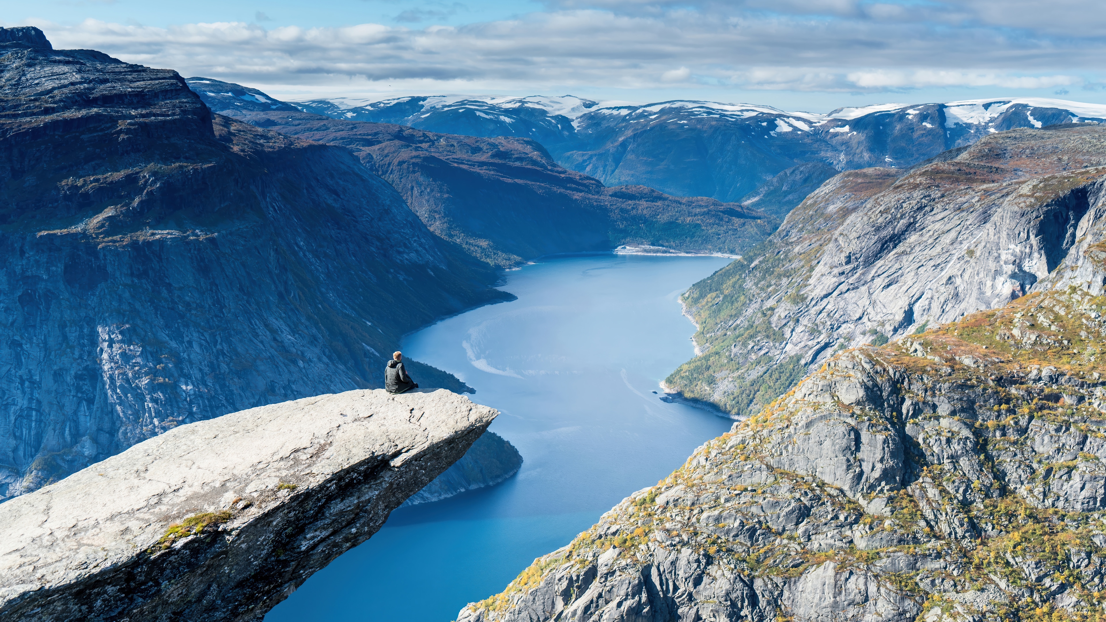 Man sitting on Trolltunga rock overlooking a fjord HD Wallpaper
