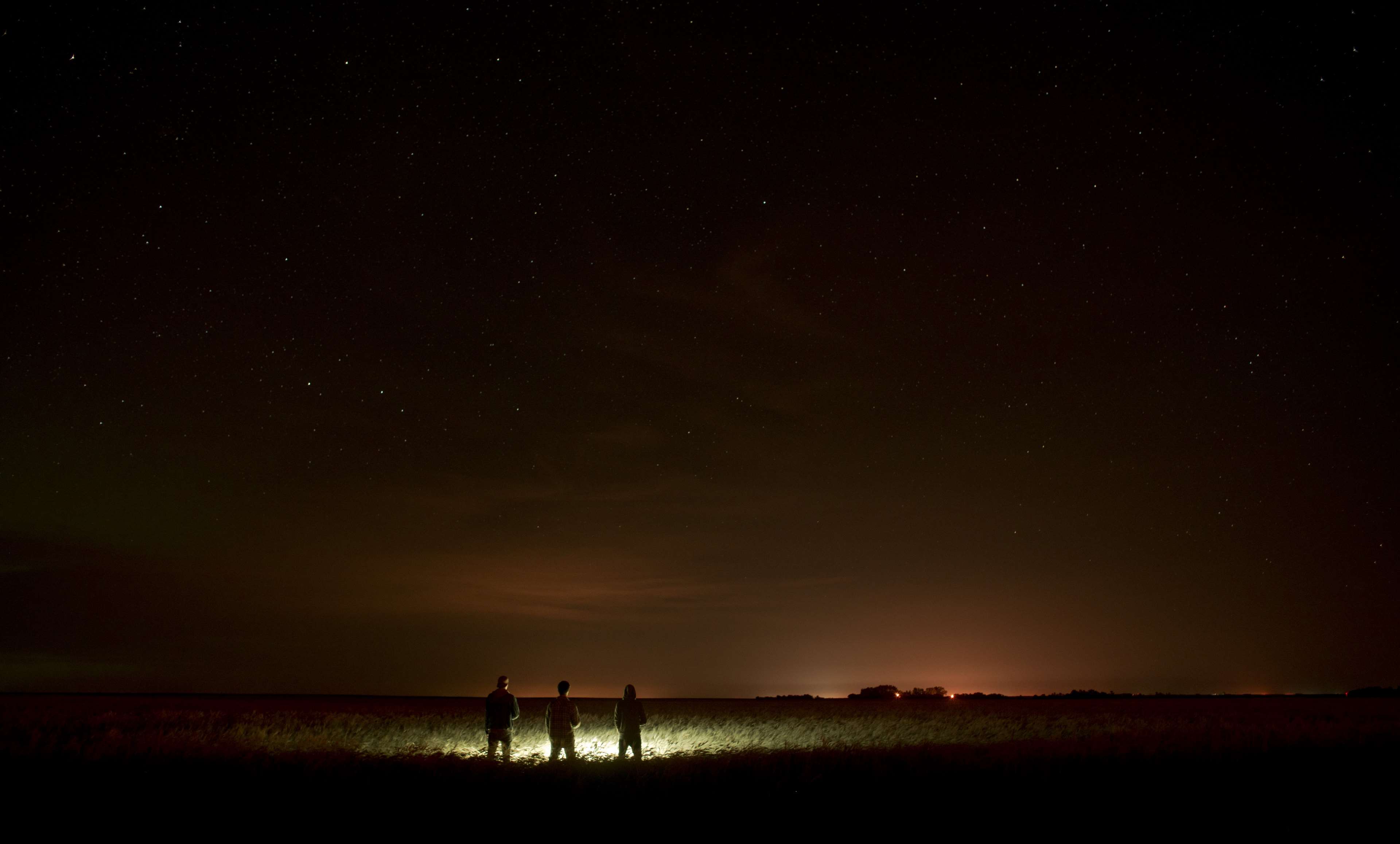 Three people stand in a field under a starry night sky HD Wallpaper