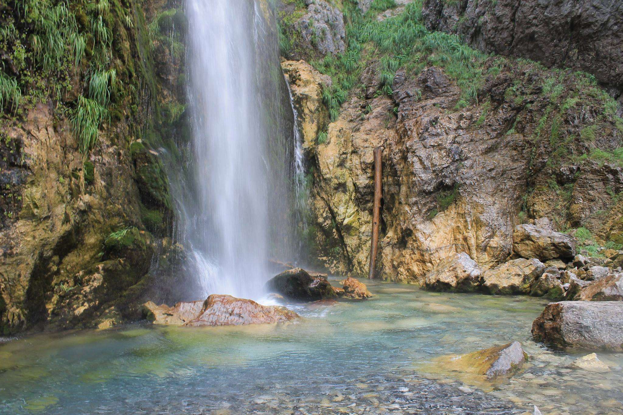 Waterfall cascading down a rocky cliff into a clear pool HD Wallpaper