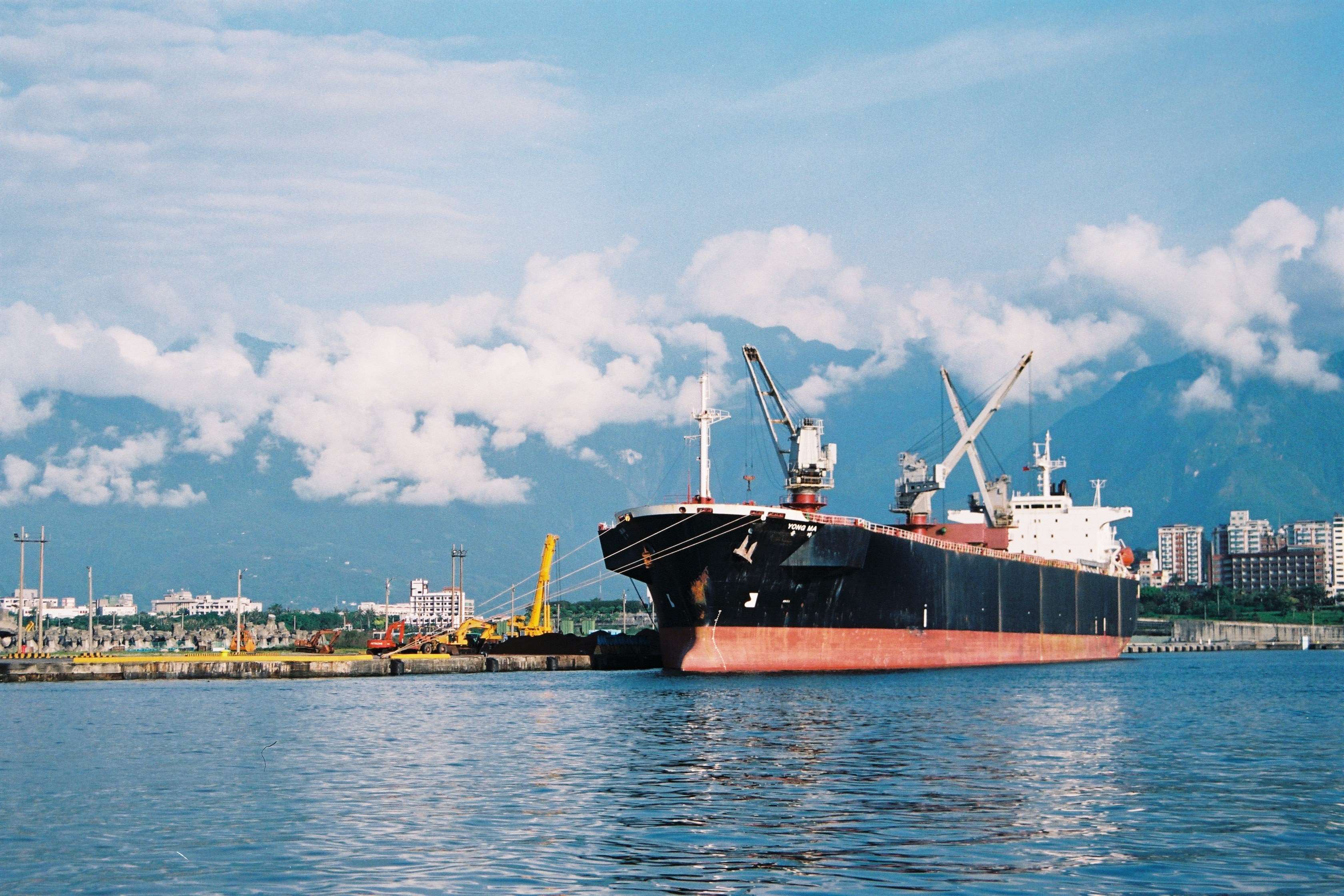 Cargo ship docked in a port with cityscape and mountains HD Wallpaper