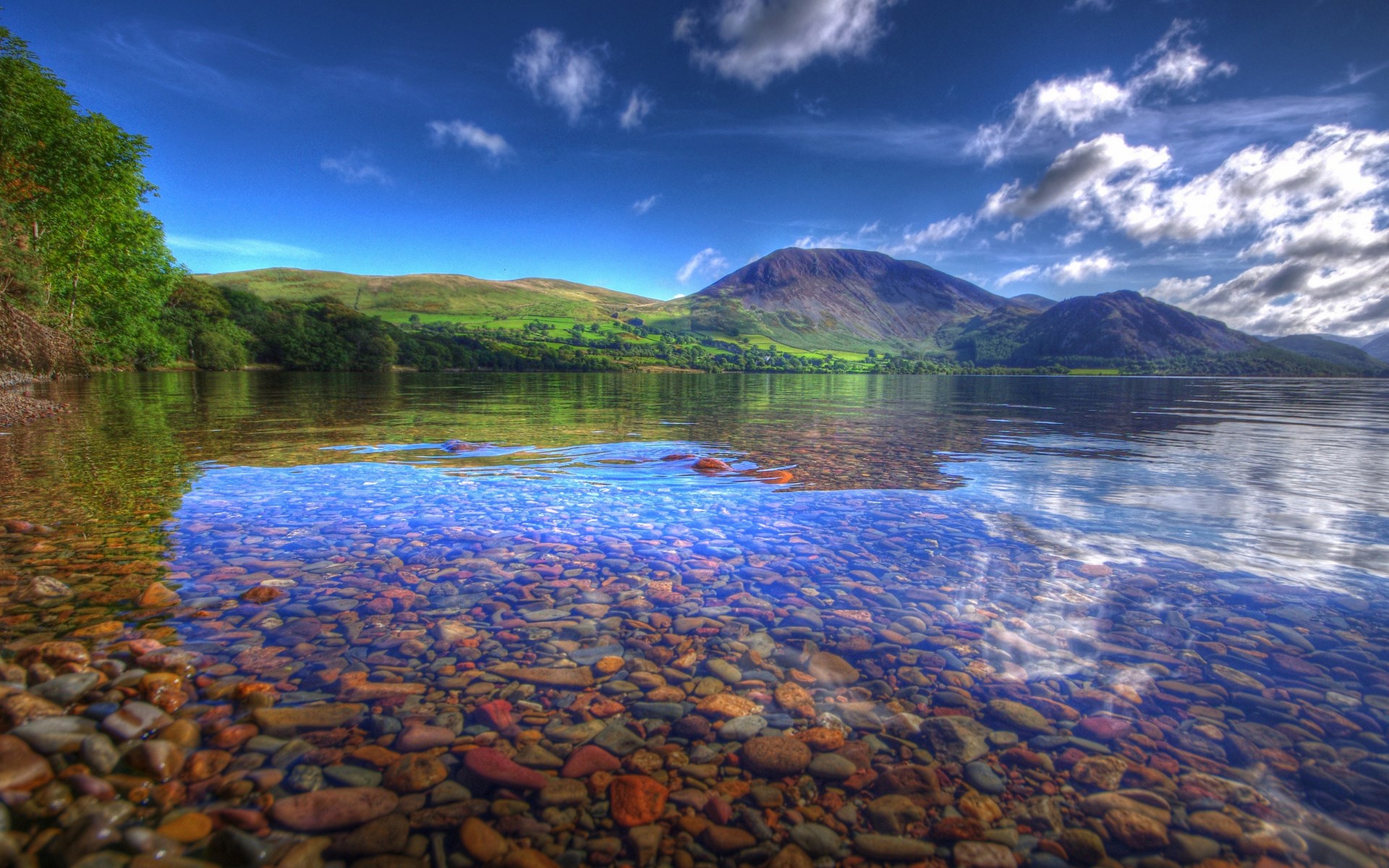Clear lake water with pebbles and mountains in the background HD Wallpaper