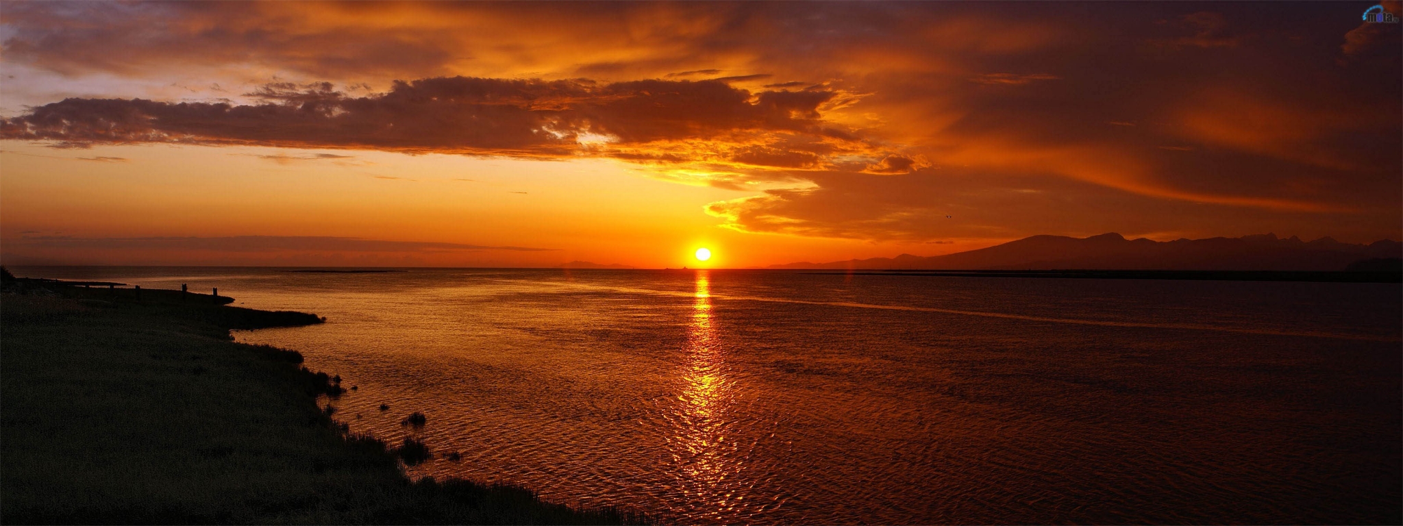 Panoramic sunset over a calm sea with mountains in the distance HD Wallpaper