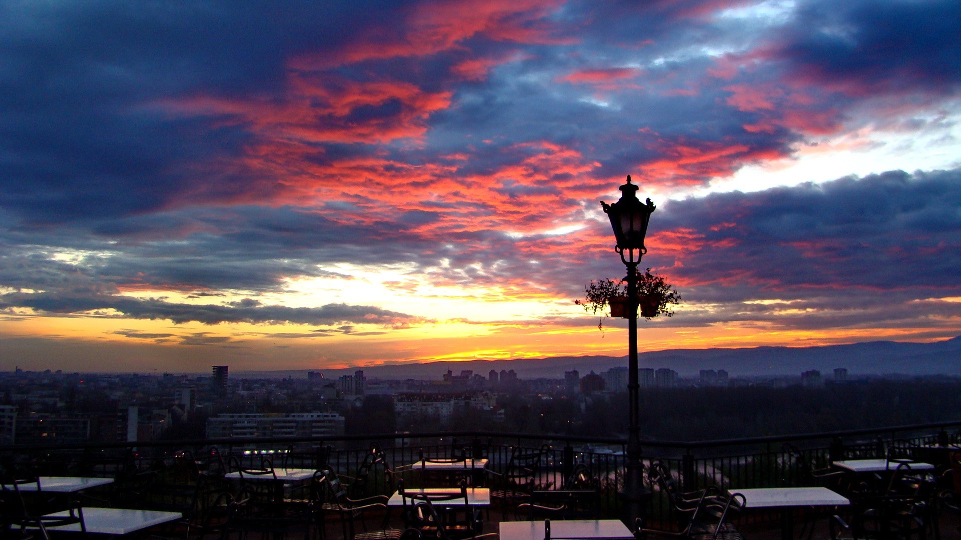 Cityscape at sunset with colorful clouds and a lamppost HD Wallpaper