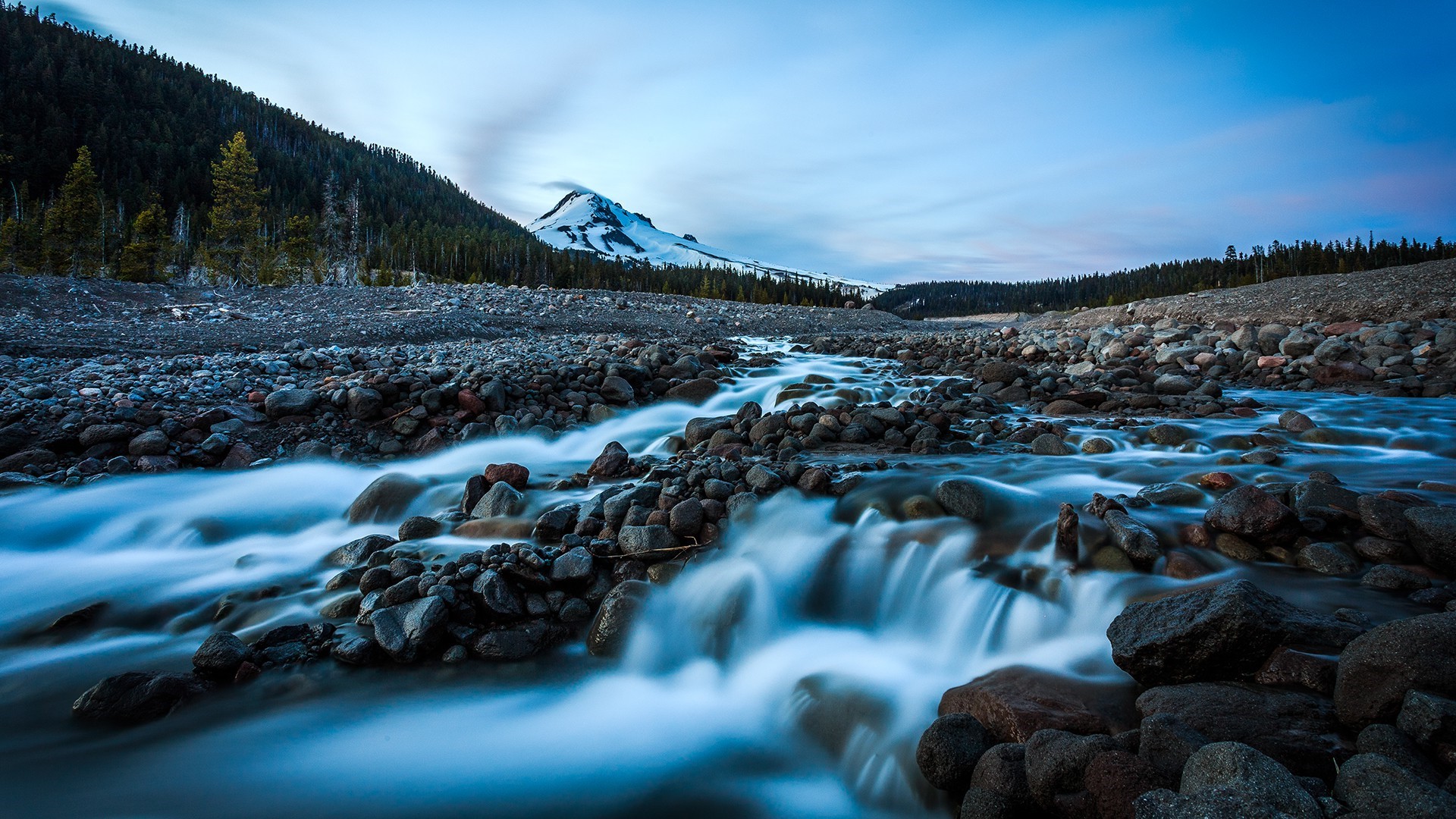 Mountain stream flowing over rocks with snow-capped mountain in background HD Wallpaper