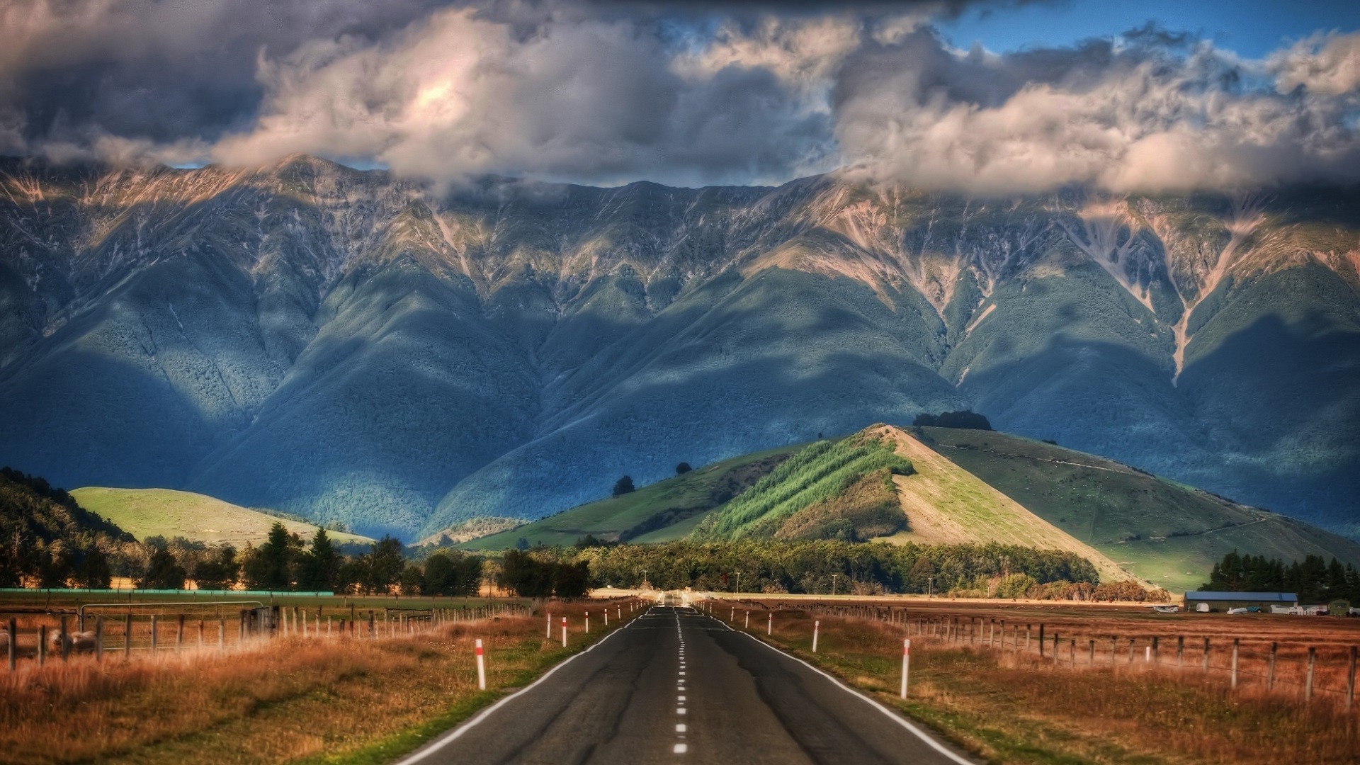 Road leading to mountains under clouds in New Zealand HD Wallpaper