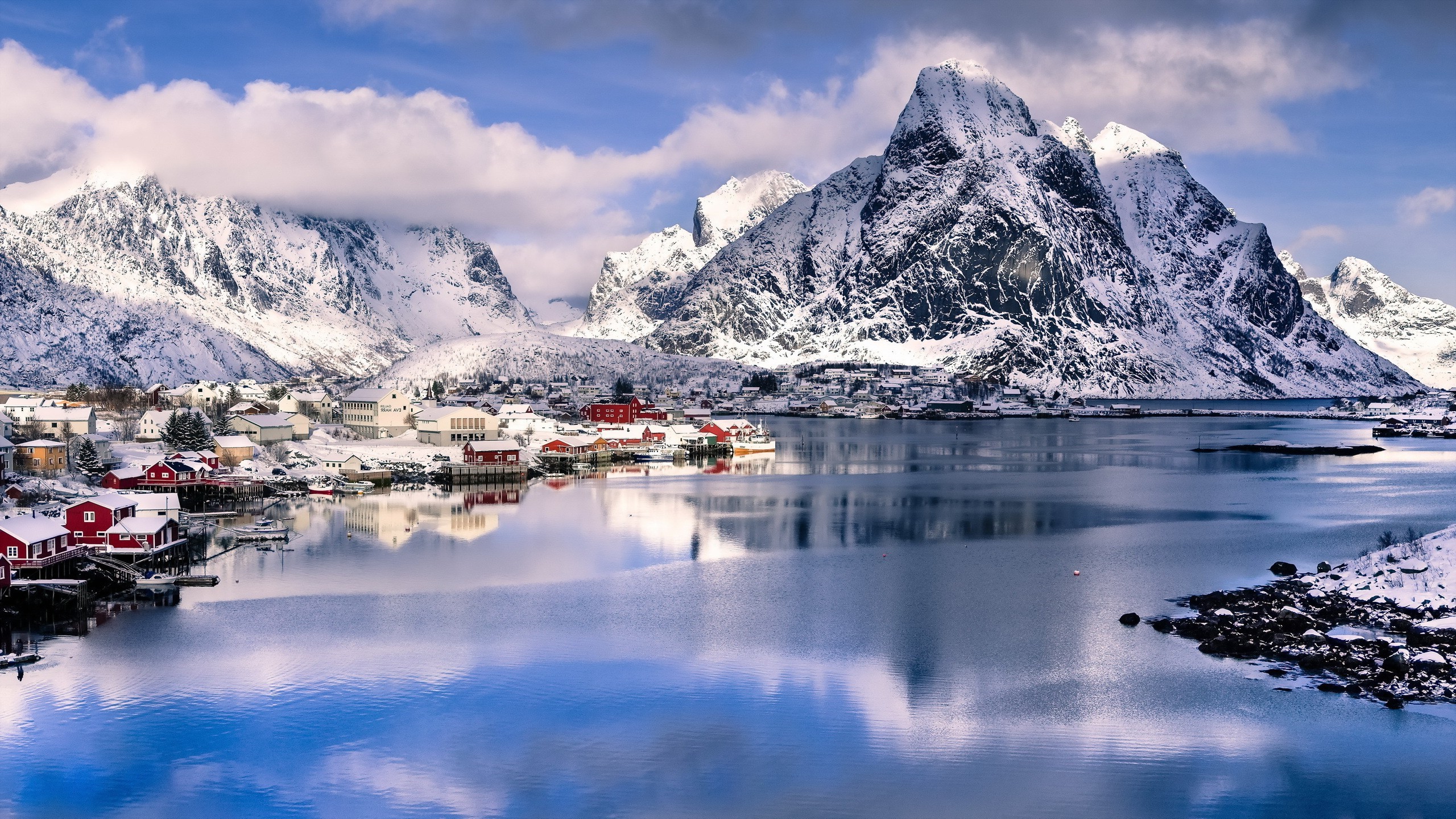 Snowy mountains overlooking a village by the water HD Wallpaper