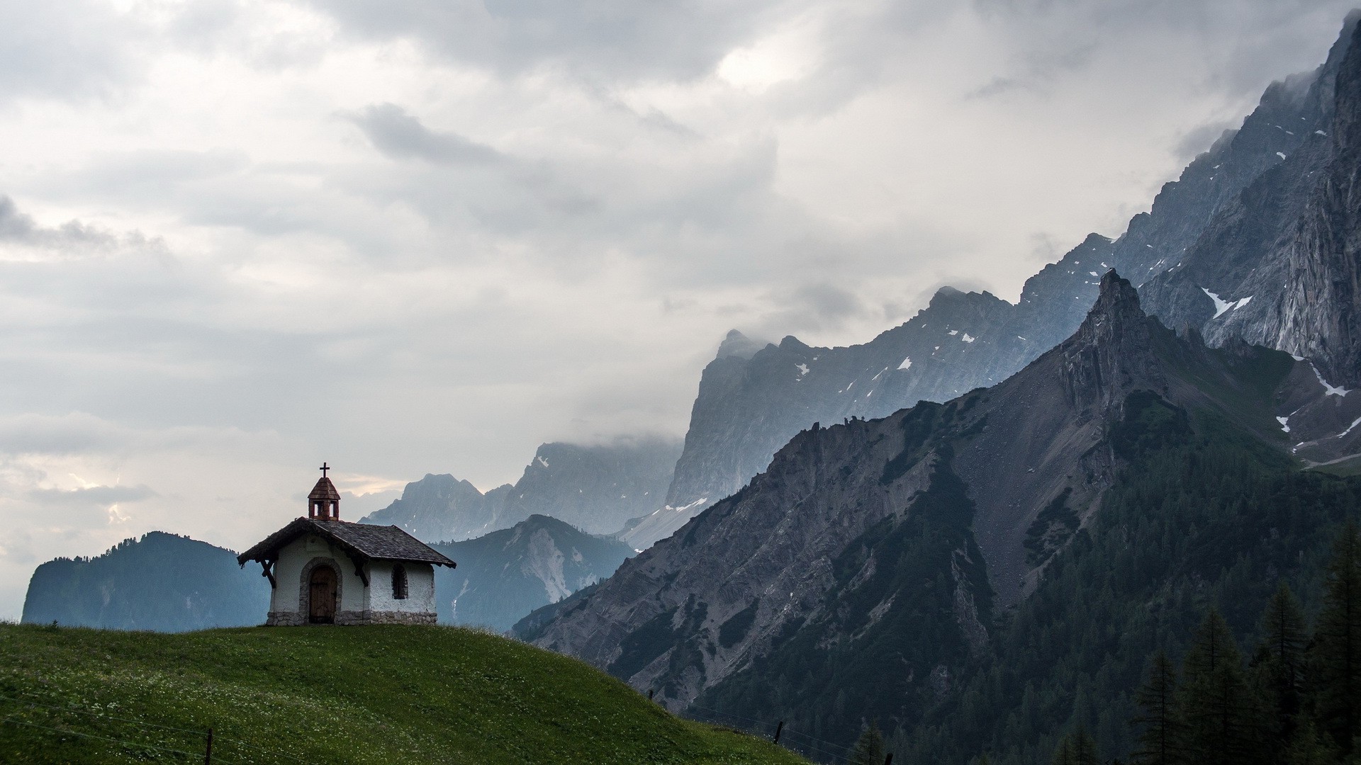 Small church on a grassy hill with mountains HD Wallpaper