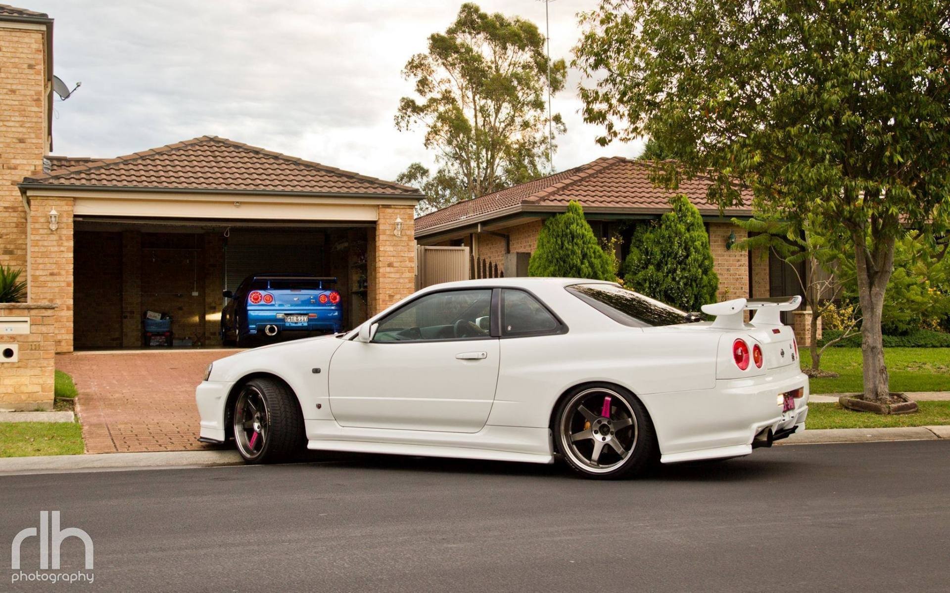 White Nissan Skyline GT-R R34 and blue Nissan Skyline in driveway HD Wallpaper