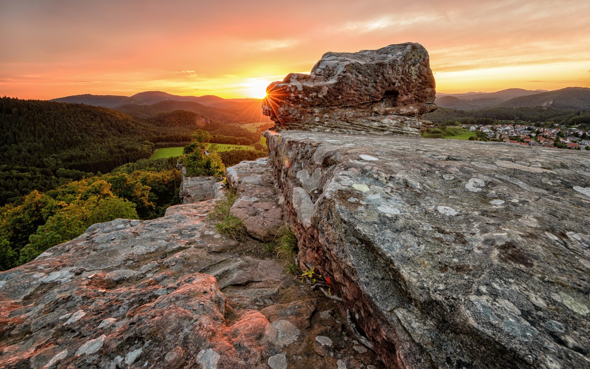 Sunset over rocky outcrop overlooking a valley and village HD Wallpaper
