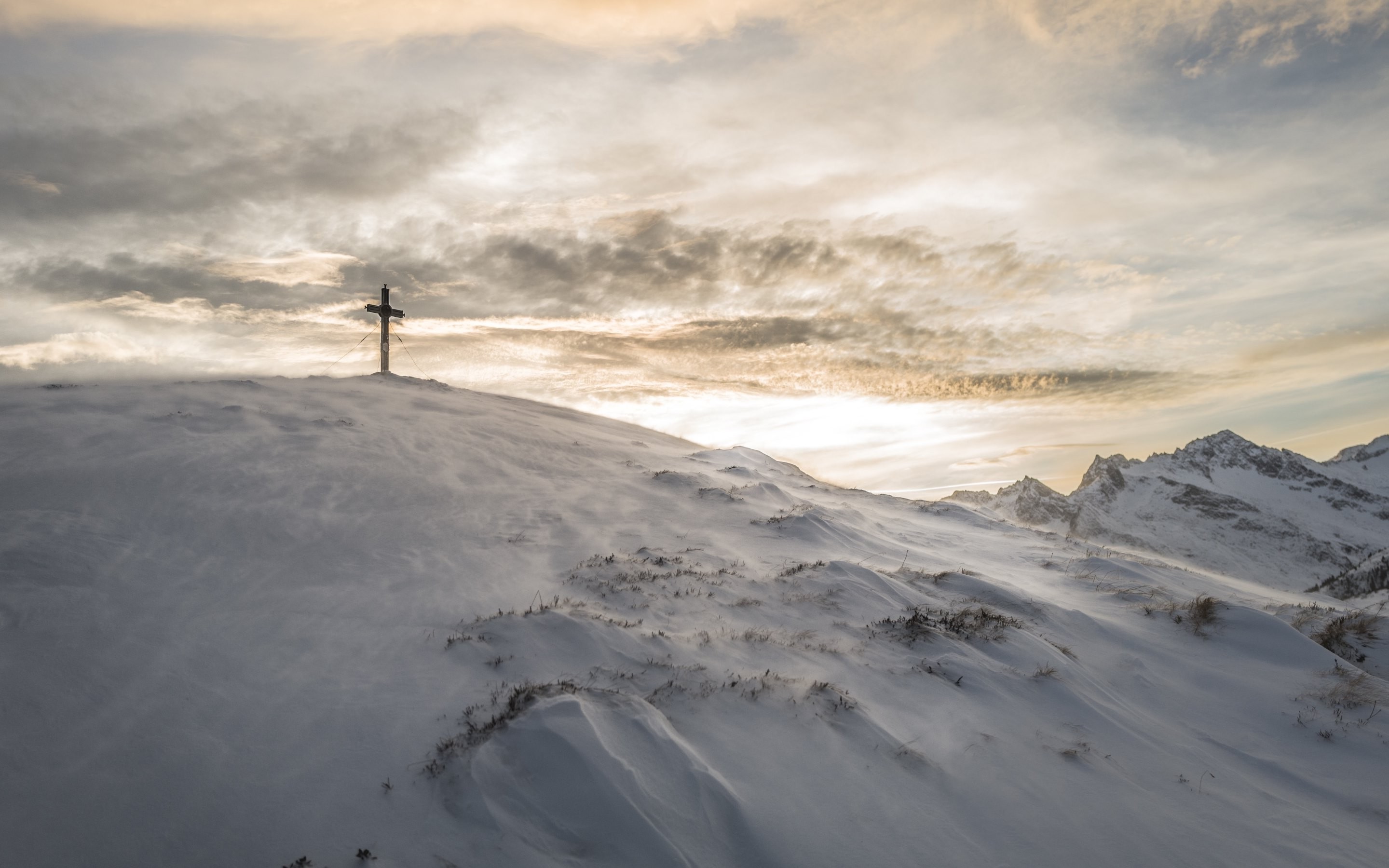 Cross on snowy mountain peak with dramatic clouds HD Wallpaper
