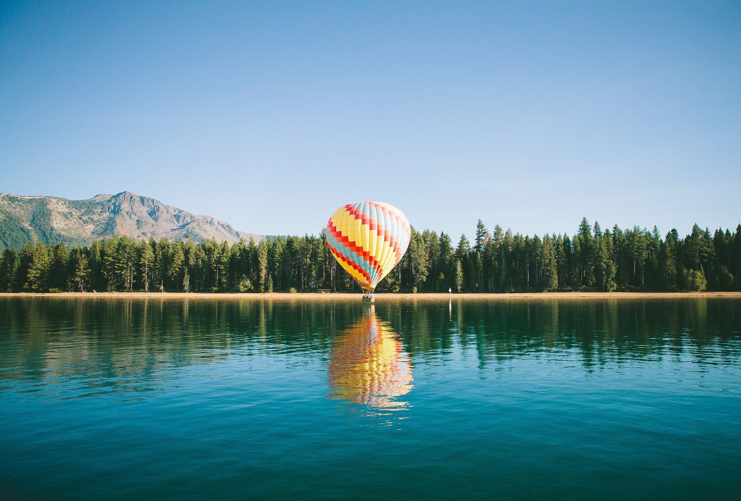 Hot air balloon over a lake with mountains and trees HD Wallpaper
