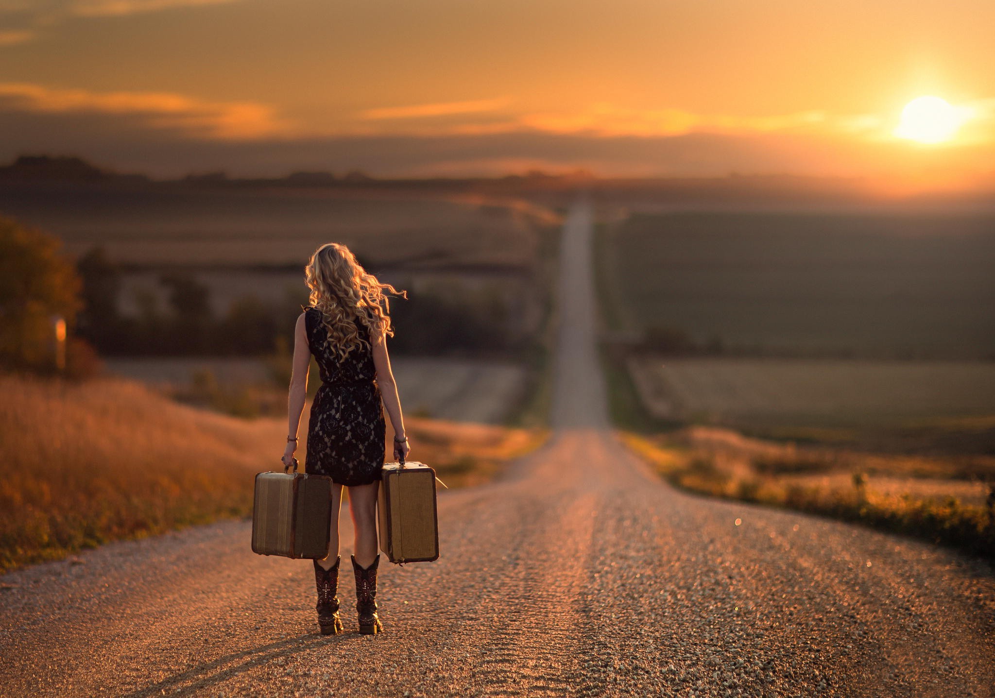 Woman with suitcases walking on a road at sunset HD Wallpaper